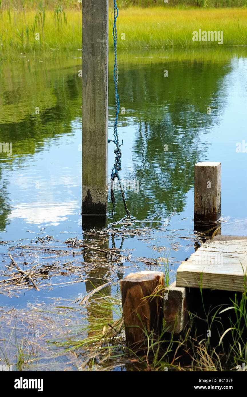 An old wooden dock pier in a salt marsh in Connecticut with cumulus clouds reflected in the blue water Stock Photo