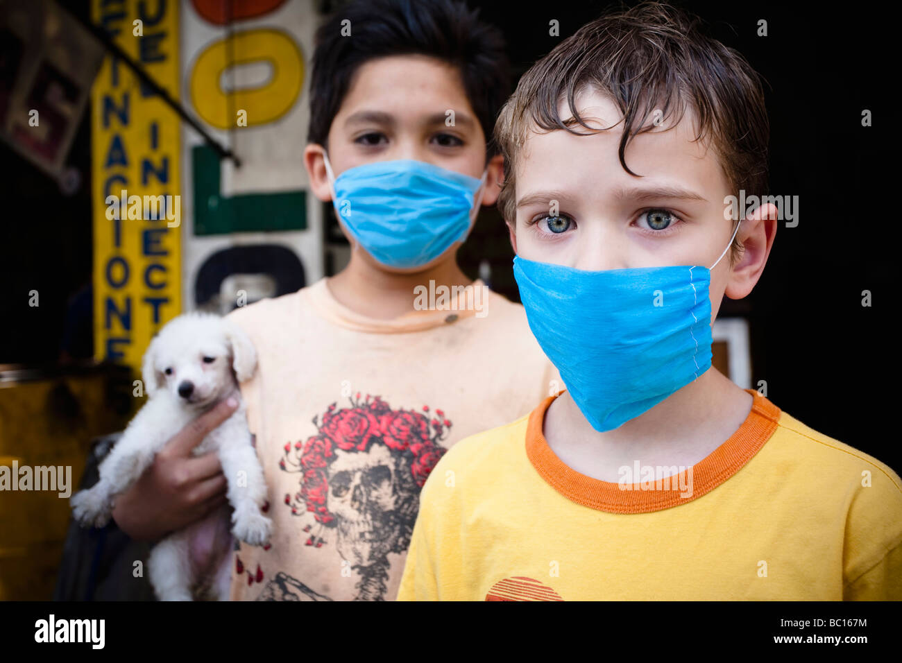Portrait of two kids wearing masks holding a small puppy in the street during the swine flu epidemic in Mexico city, DF, Mexico. Stock Photo
