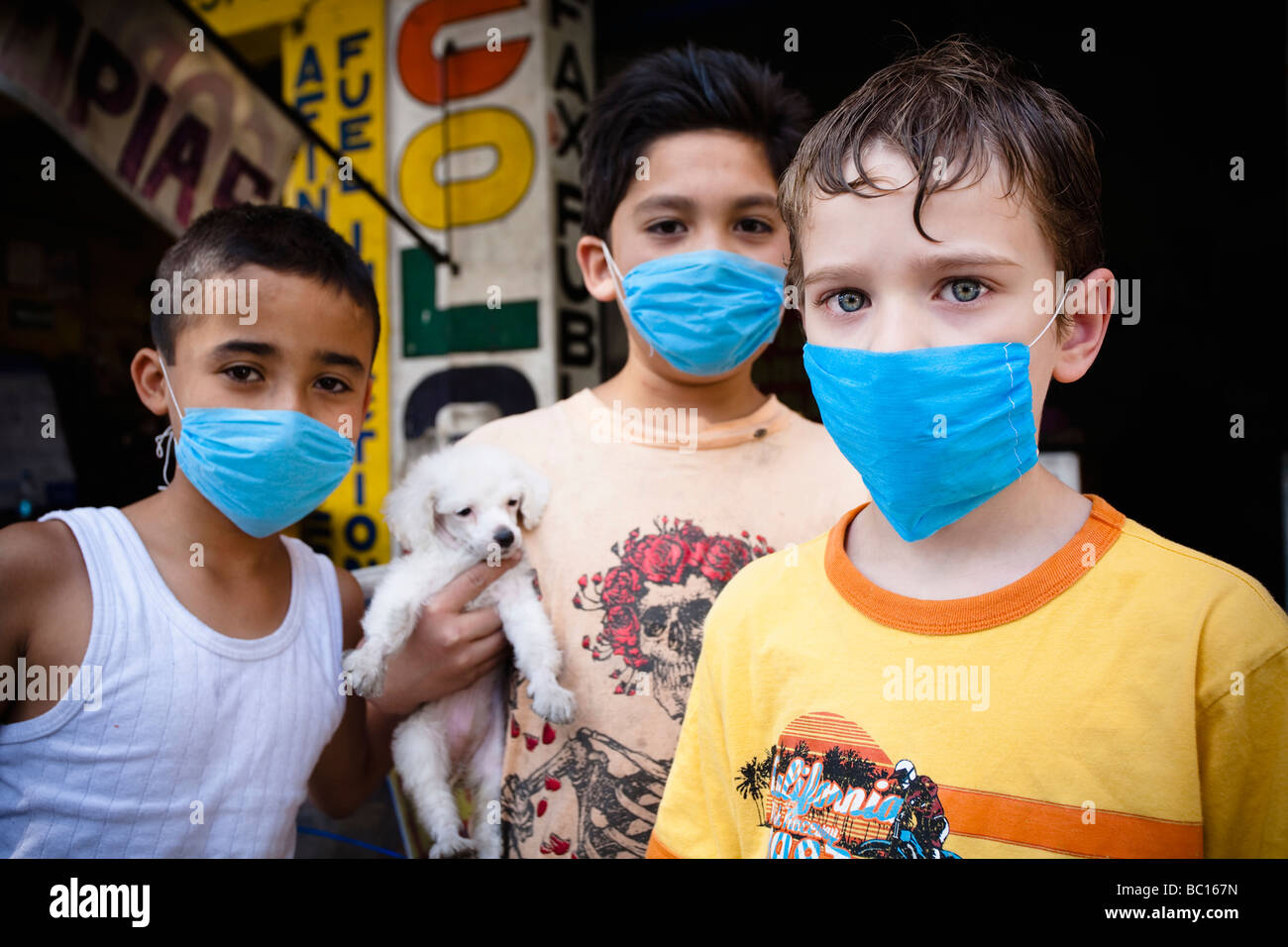 Portrait of three kids wearing masks  holding a small puppy in the street during the swine flu epidemic in Mexico city, DF, Mexi Stock Photo
