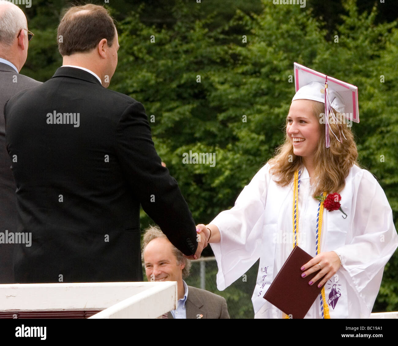 Graduation ceremony, female high school student in cap and gown accepts diploma Stock Photo