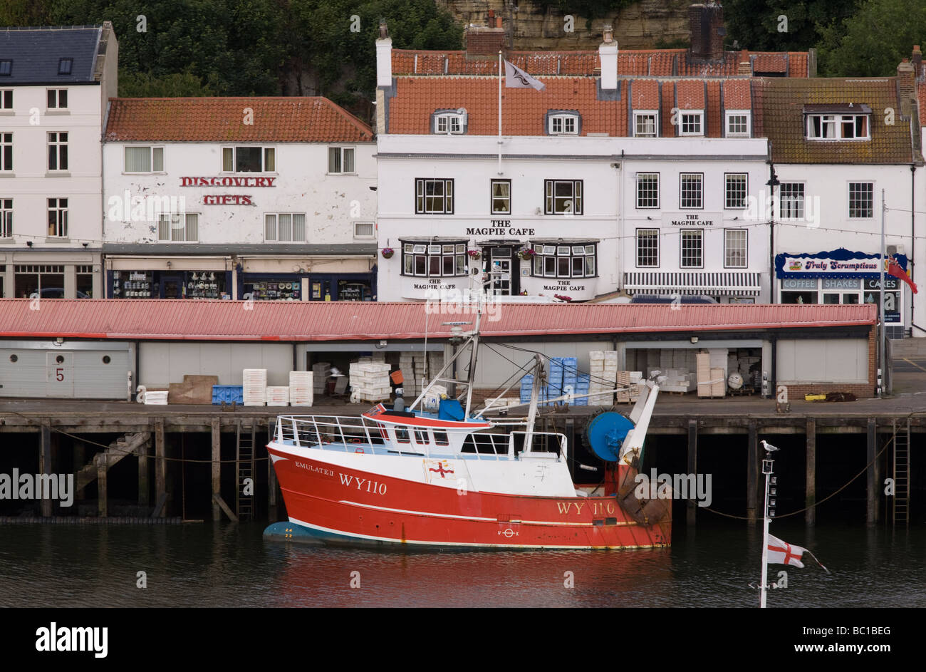 A fishing trawler moored in front of the fish quay and the Magpie Cafe, famous fish and chip restaurant - Whitby Stock Photo