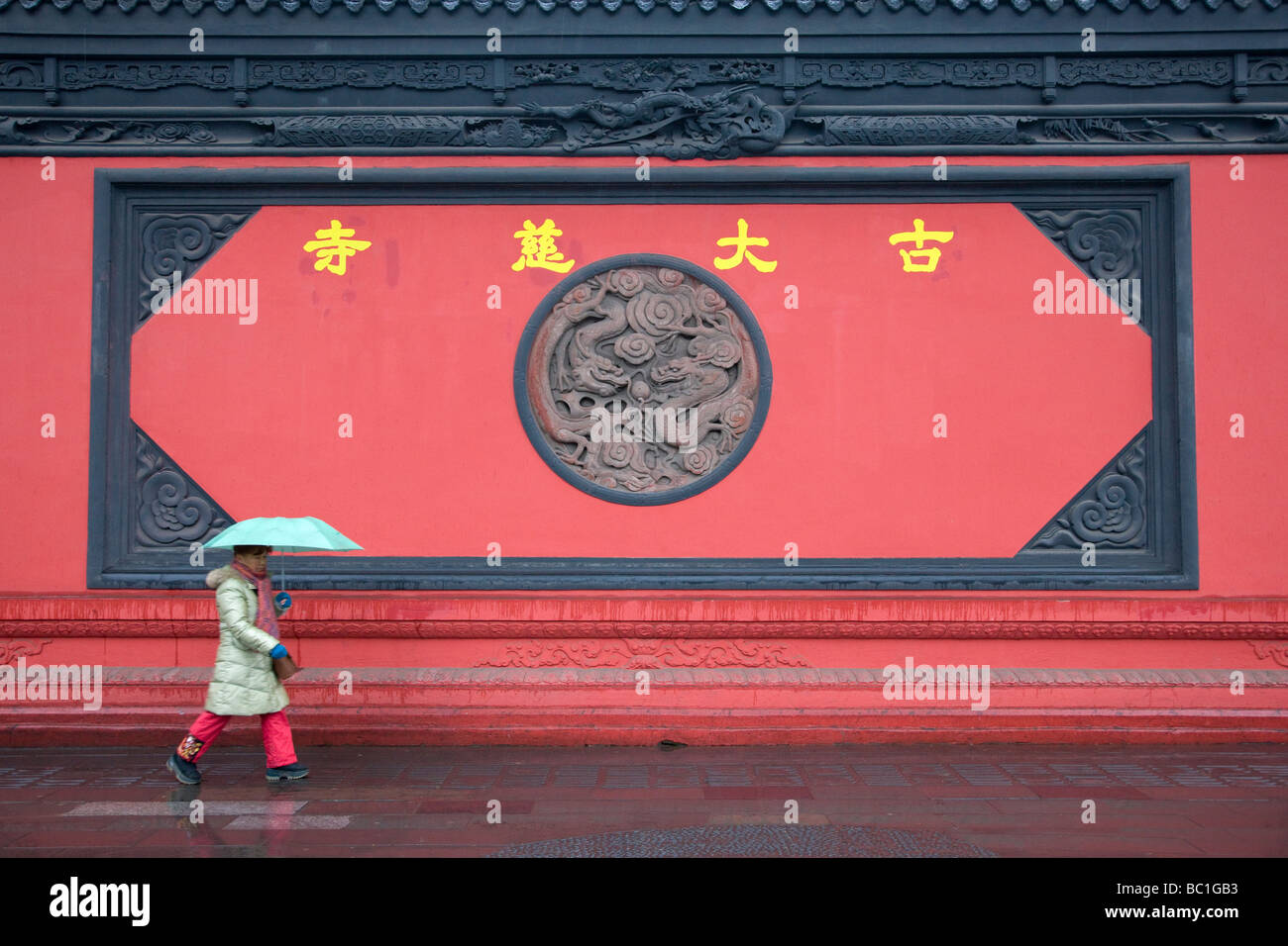 Woman with umbrella walk by the red wall of Gudaci Temple Chengdu Sichuan China Stock Photo