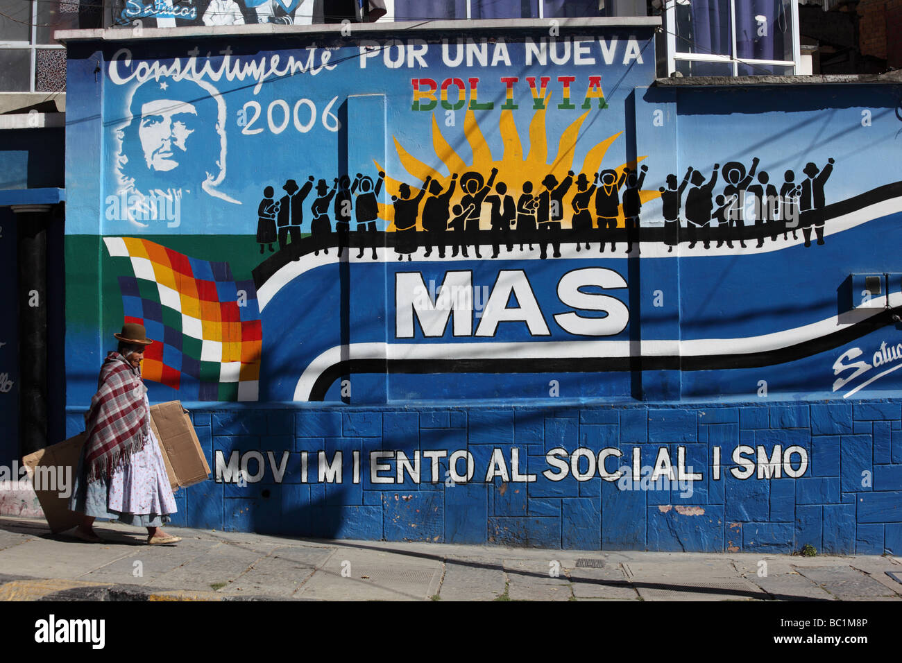 Elderly Aymara lady or cholita passing Movimiento al Socialismo political party mural on wall, La Paz , Bolivia Stock Photo