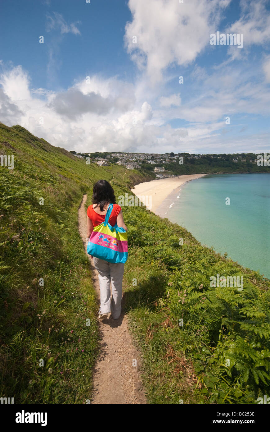 Woman with colourful beach bag walking along the coastal path in Cornwall approaching Carbis Bay. Stock Photo