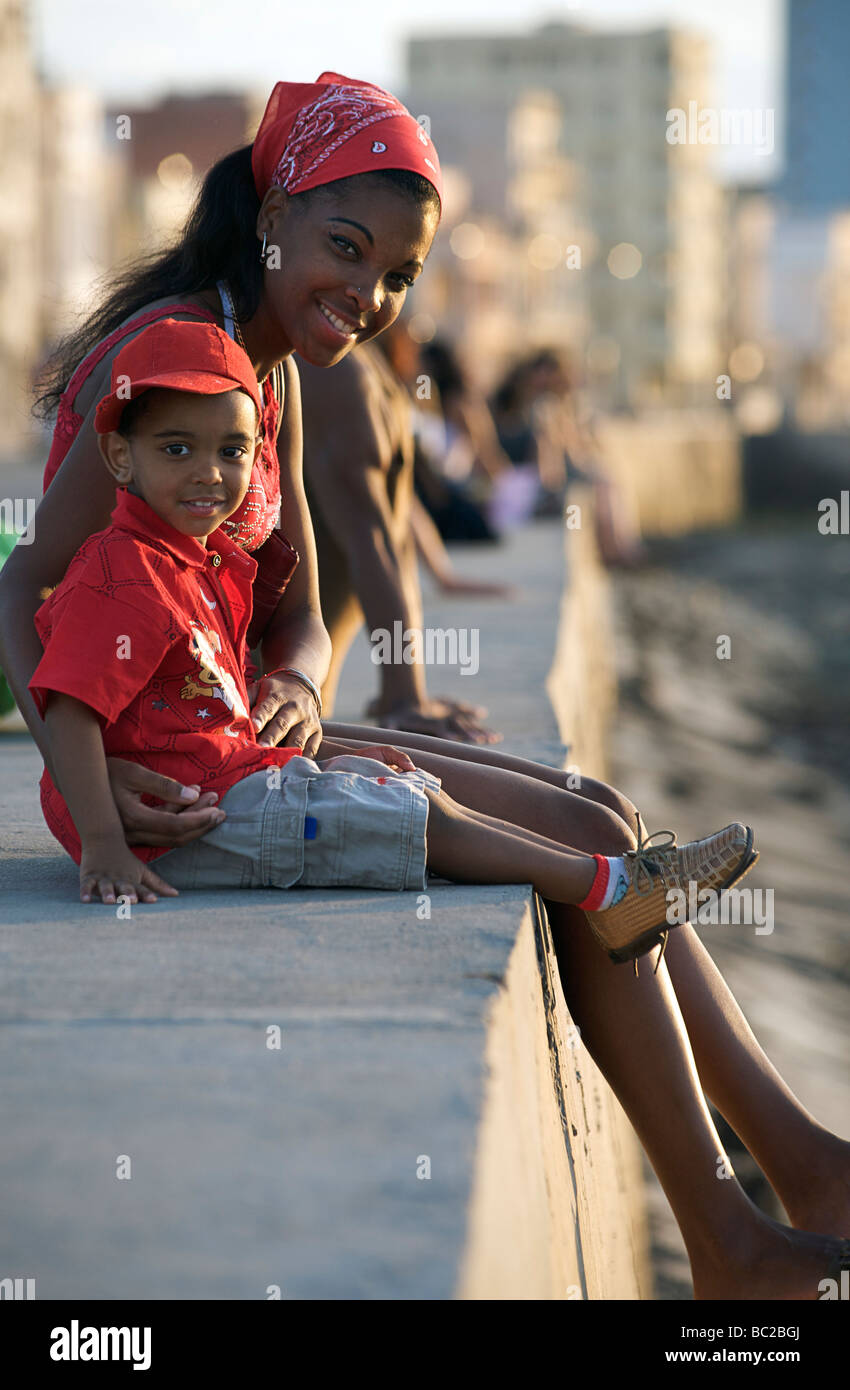 Young Cuban woman with child sitting on the seawall at the Malecon. Havana, Cuba Stock Photo