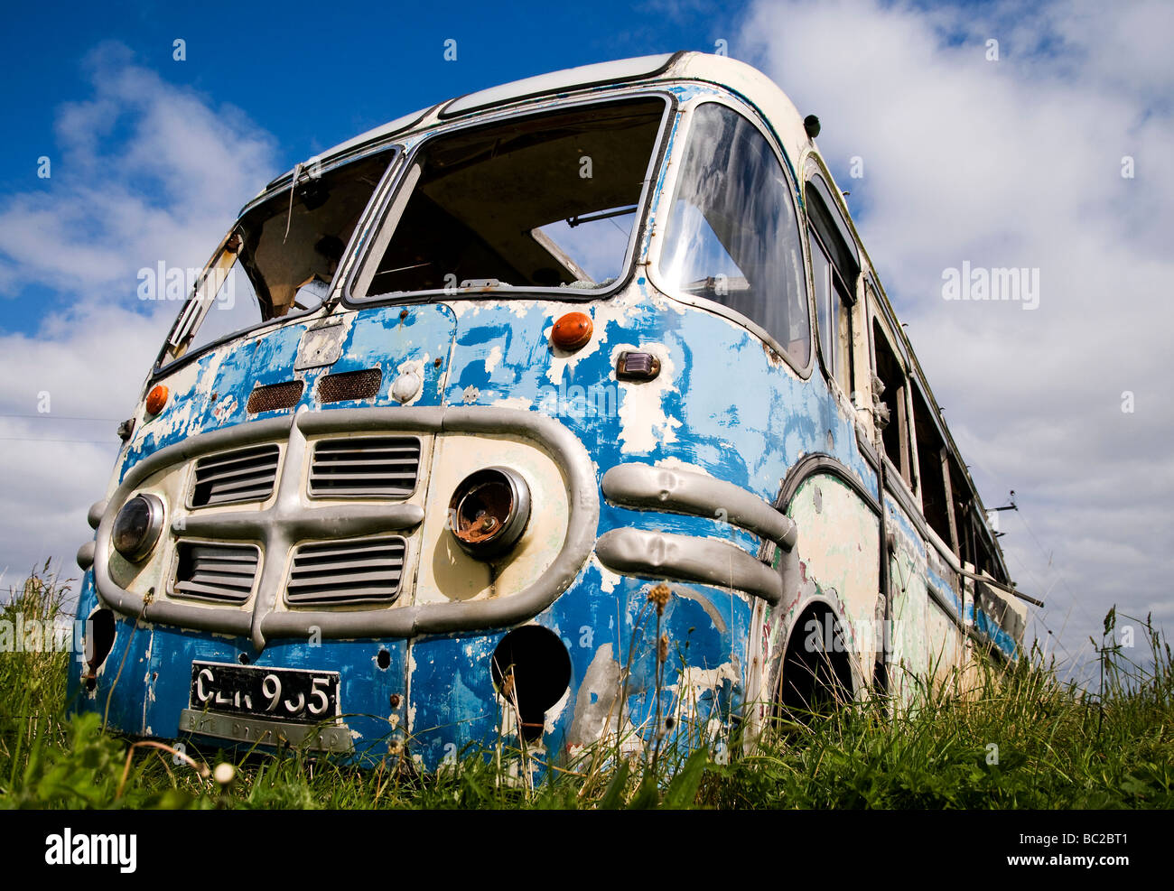 derelict wreck of a vintage blue bus with broken windows and grass growing through projecting feeling of adventure and hippie Stock Photo