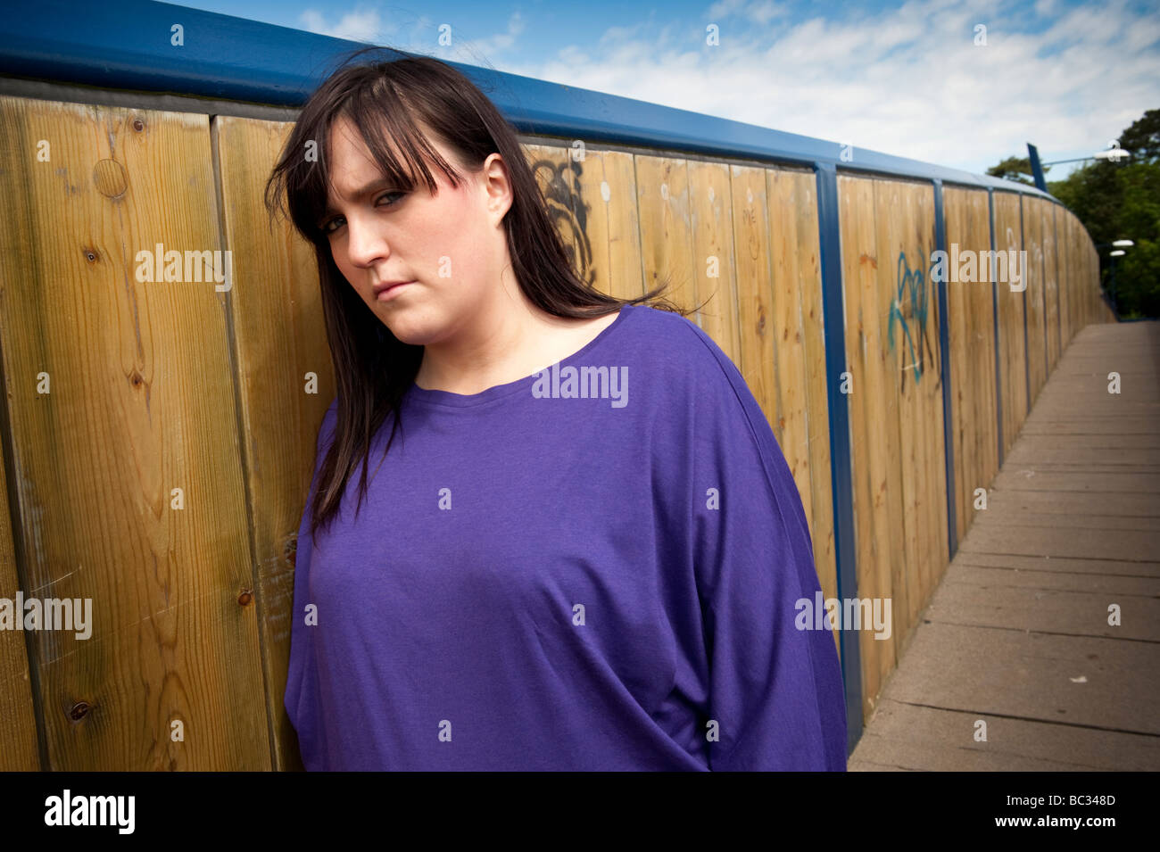 Sad depressed young overweight woman 18 to 21 year old standing on walkway bridge Stock Photo
