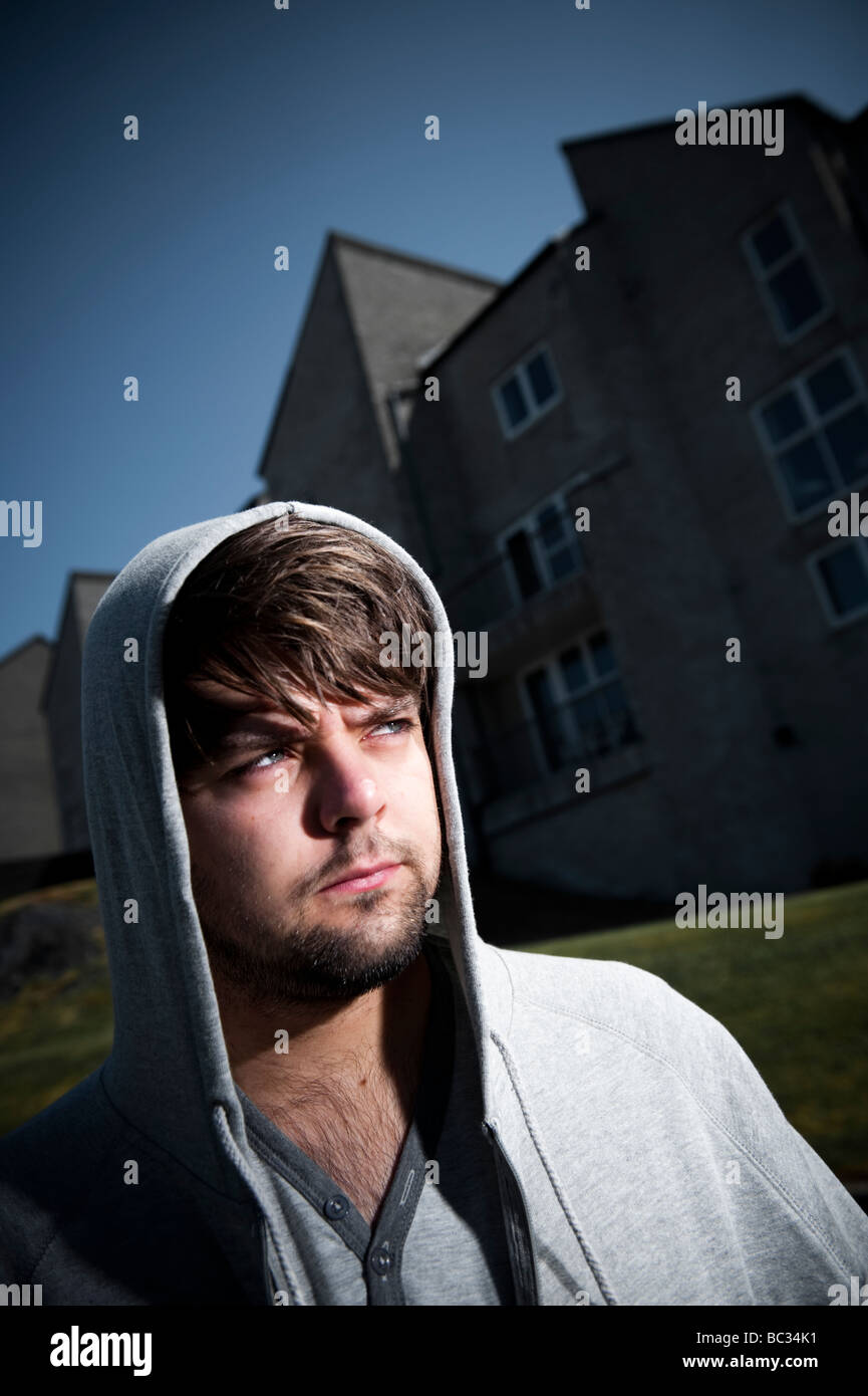 Young man wearing hoodie standing outside a block of flats, alone looking worried thoughtful Stock Photo