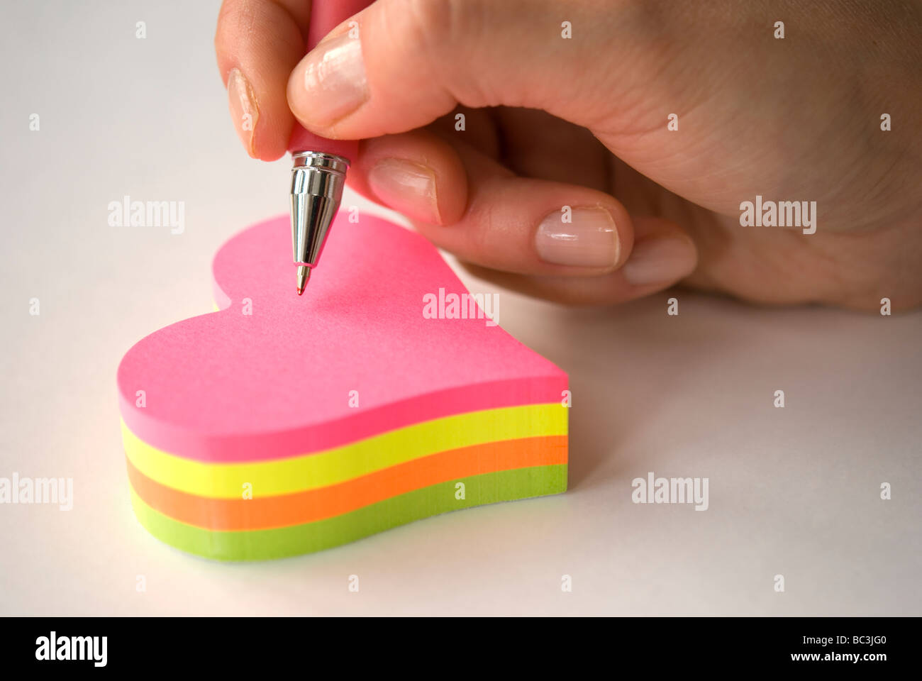 Hand holding pen writing on heart shaped colorful sticky notes Stock Photo