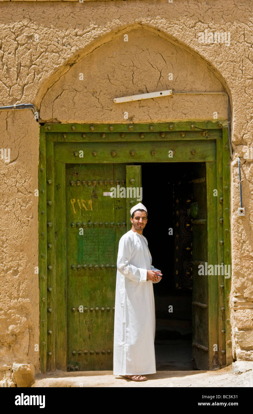 Young local man in front of traditional house made from mud and brick in the town of Al Hamra Sultanate of Oman Stock Photo