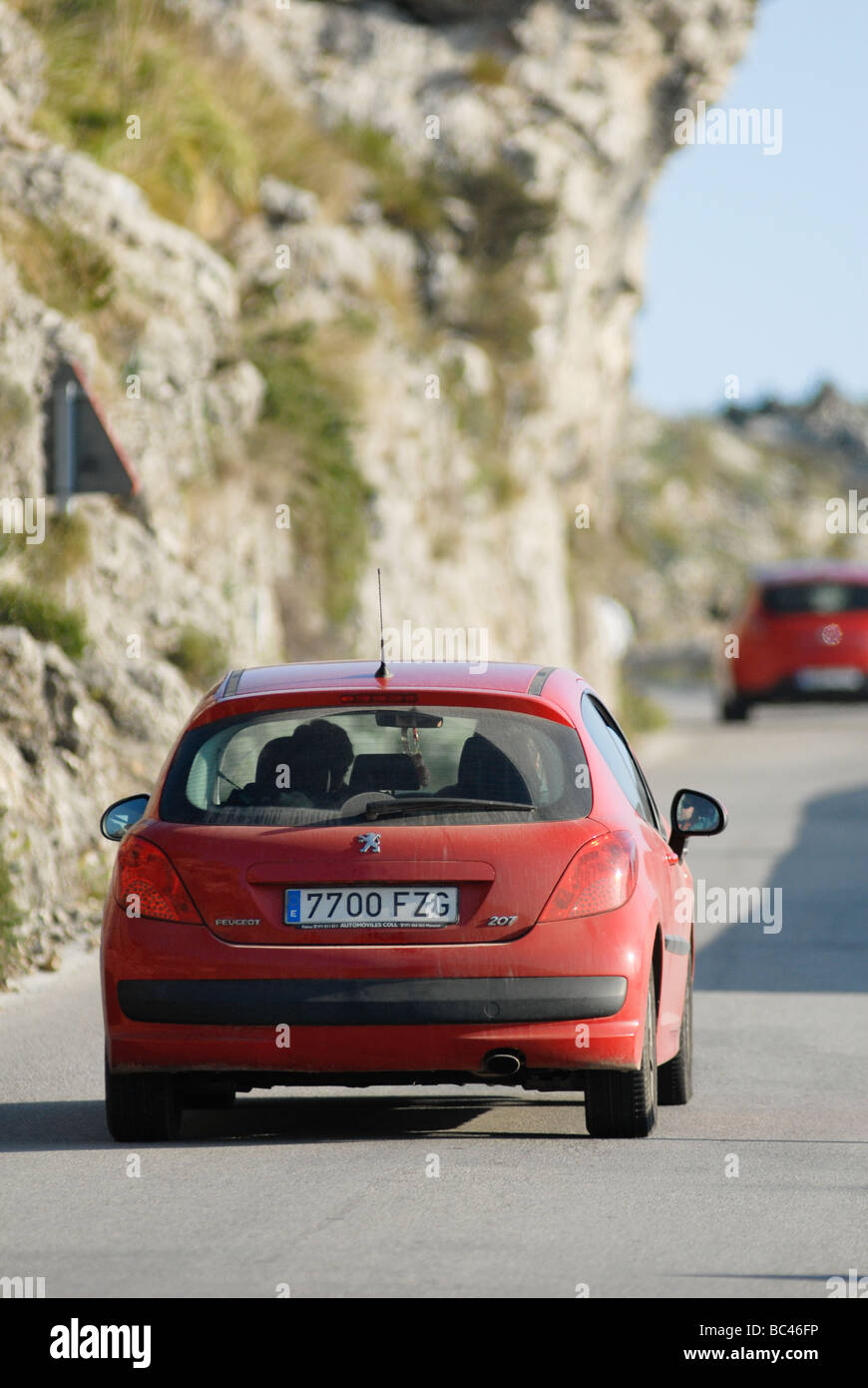 Rear view of a red peugeot 207 car driving along a road in Spain Stock Photo