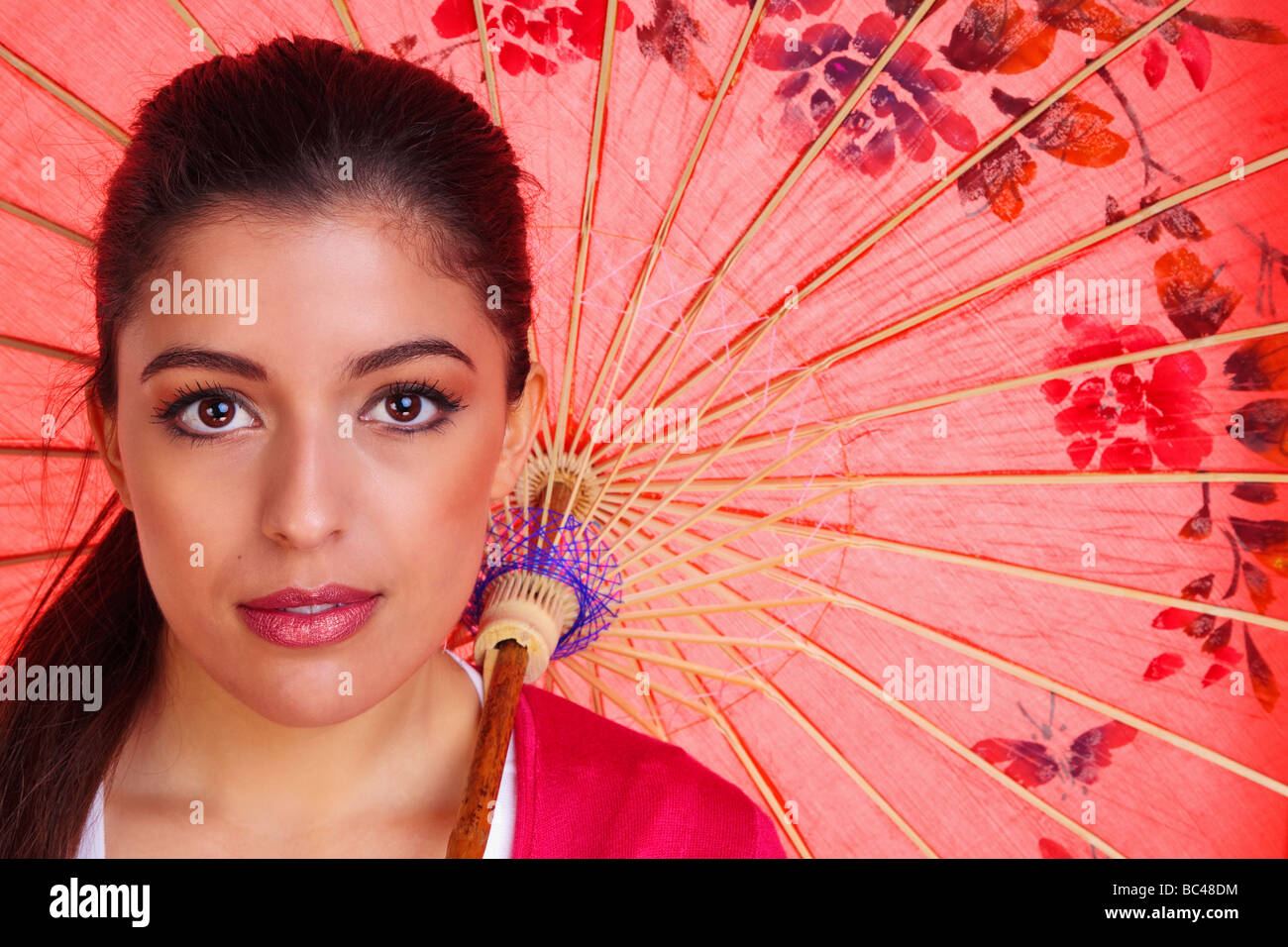 Beauty shot of a young brunette woman with brown eyes holding a red chinese umbrella Stock Photo