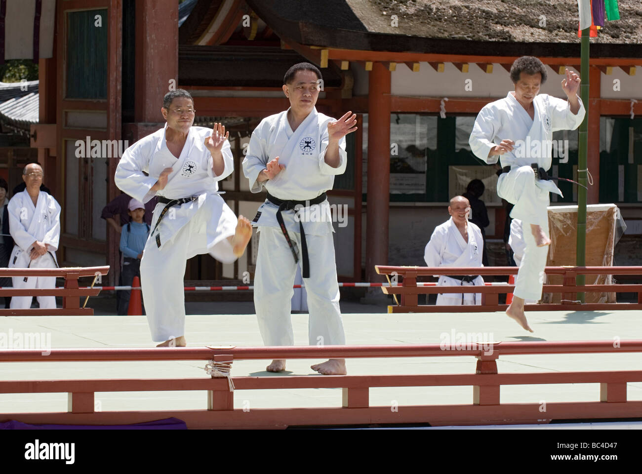 Three men wearing dogi and black belts strike a karate kicking pose
