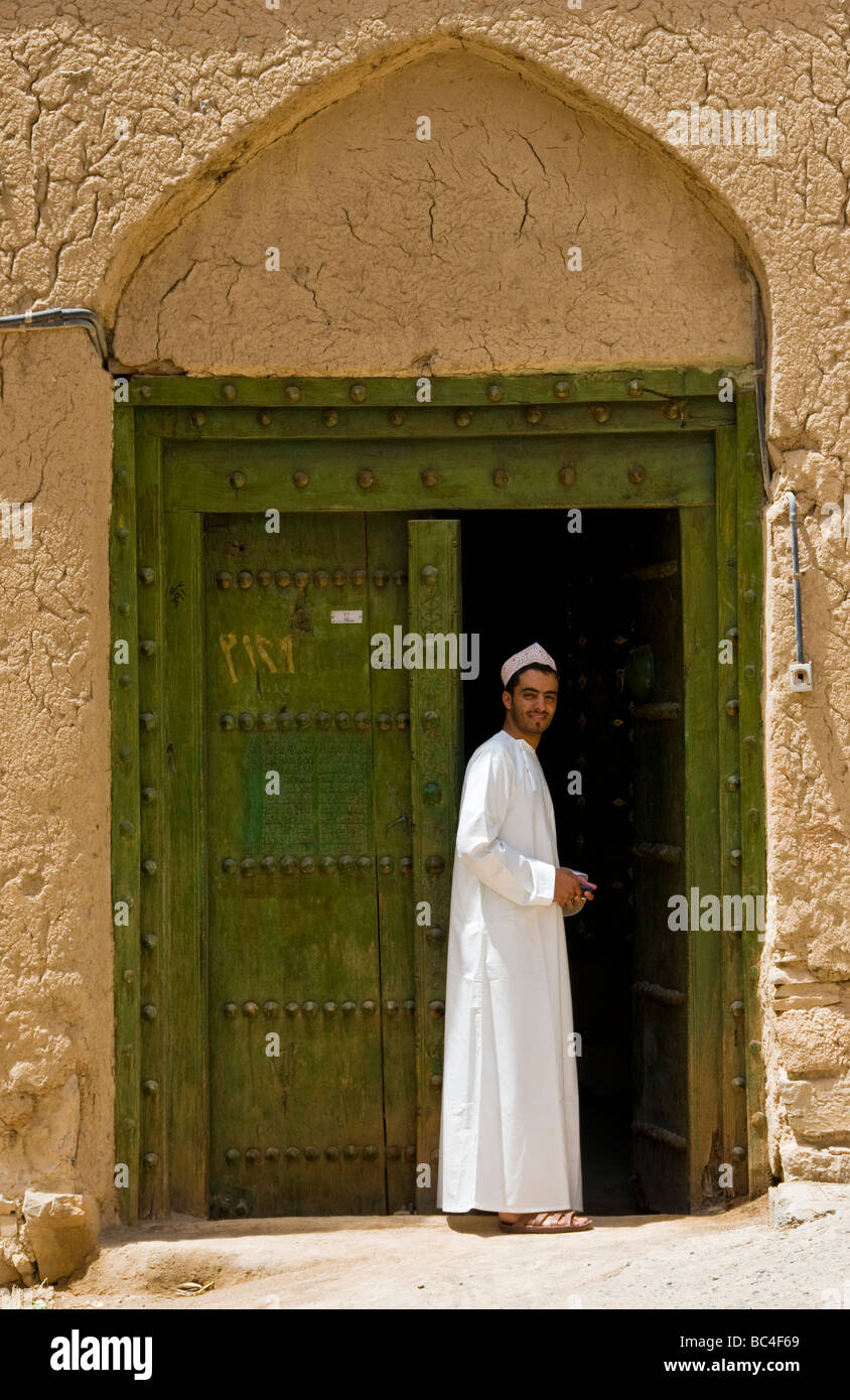 Young local man in front of traditional house made from mud and brick in the town of Al Hamra Sultanate of Oman Stock Photo