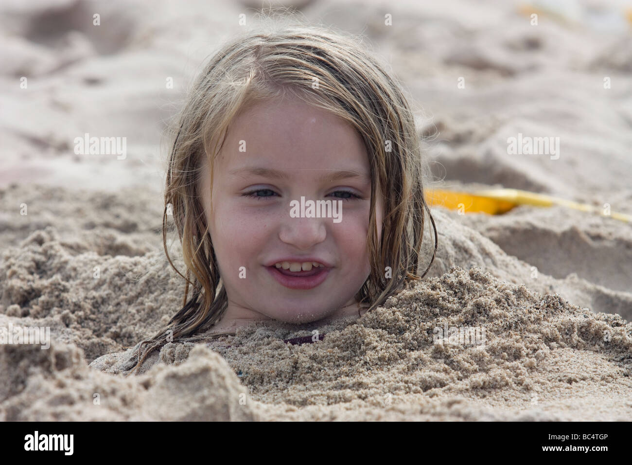 Young girl buried up to her head in sand at the beach Stock Photo