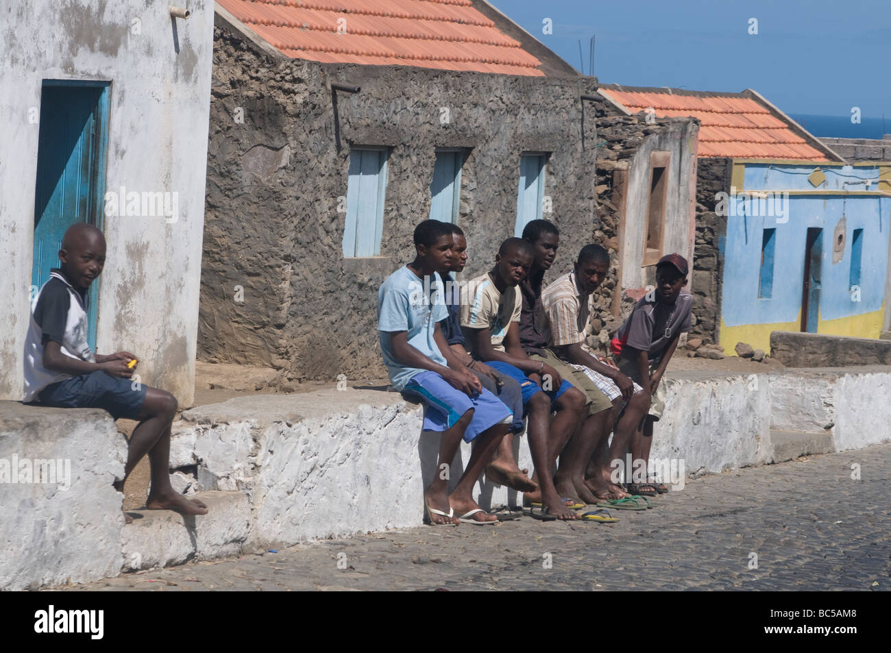 Dark skinned young men sitting on wall Santiago Cabo Verde Africa Stock Photo