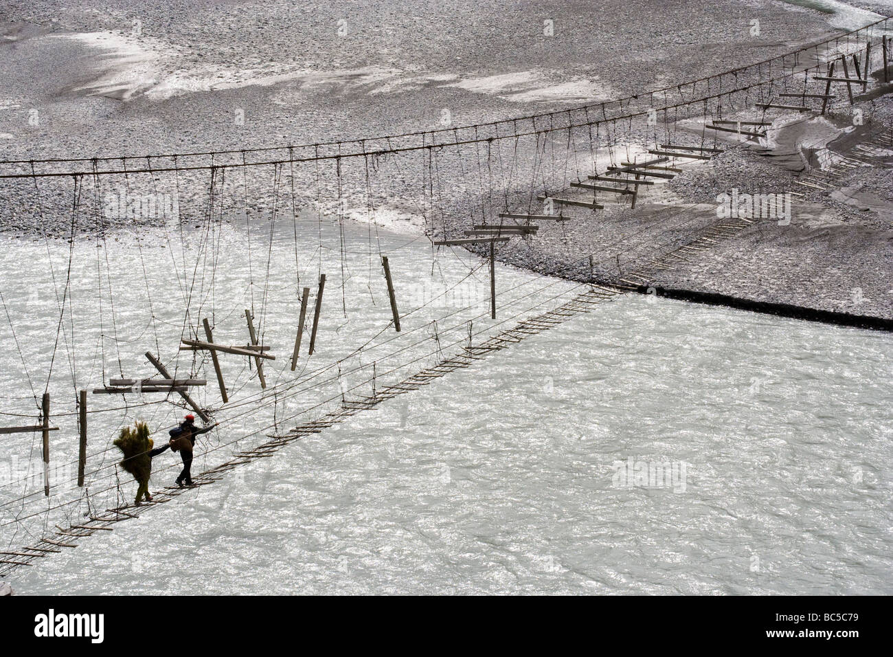 Locals crossing a delicate rope bridge over the Hunza river, Karakorum ...