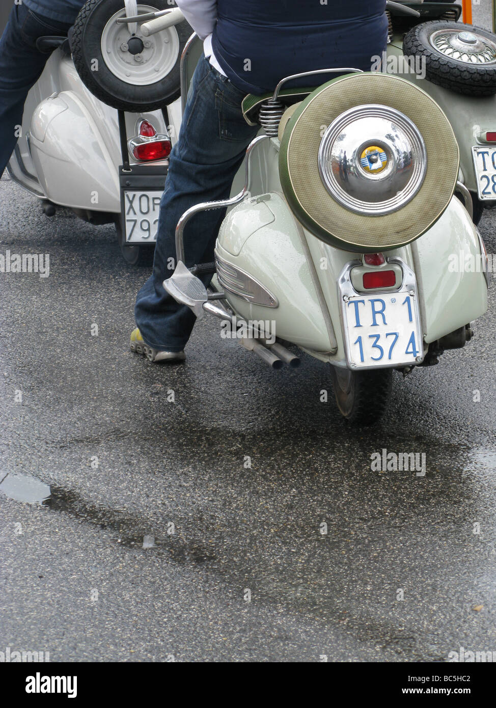 people riding old style lambretta vespa type scooters mopeds in rain in