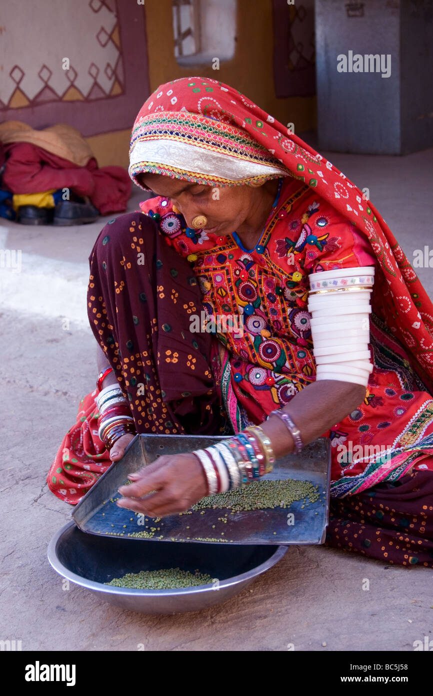 Indian Woman Sifts through Grains. She is wearing Traditional Indian Tribal Dress as mainly worn in Rajasthan & Gujarat States Stock Photo