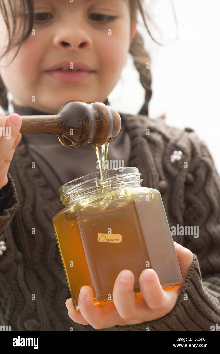 Girl taking organic honey out of jar with honey dipper Stock Photo Alamy