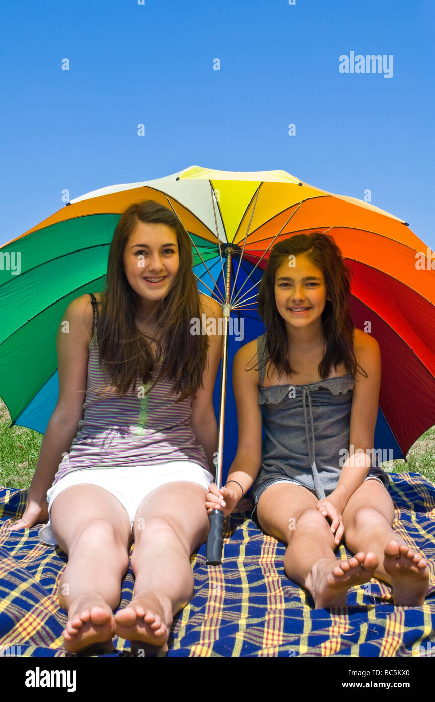 Vertical portrait of two young sisters shielding themselves from the sun underneath a huge colourful umbrella on a summer's day Stock Photo