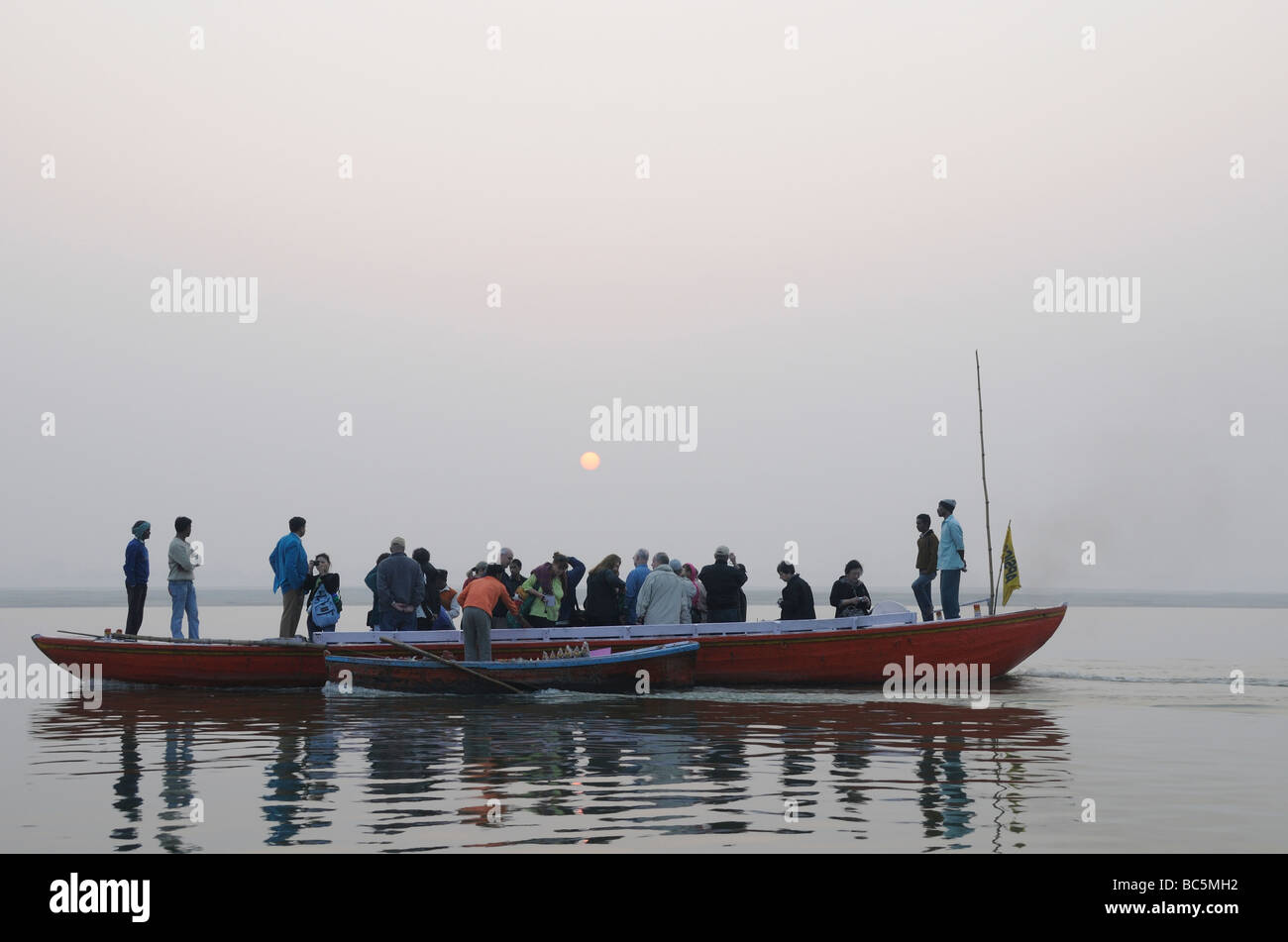 Tourists in a long rowing boat watch the sun rise over the River Ganges. Varanasi Stock Photo