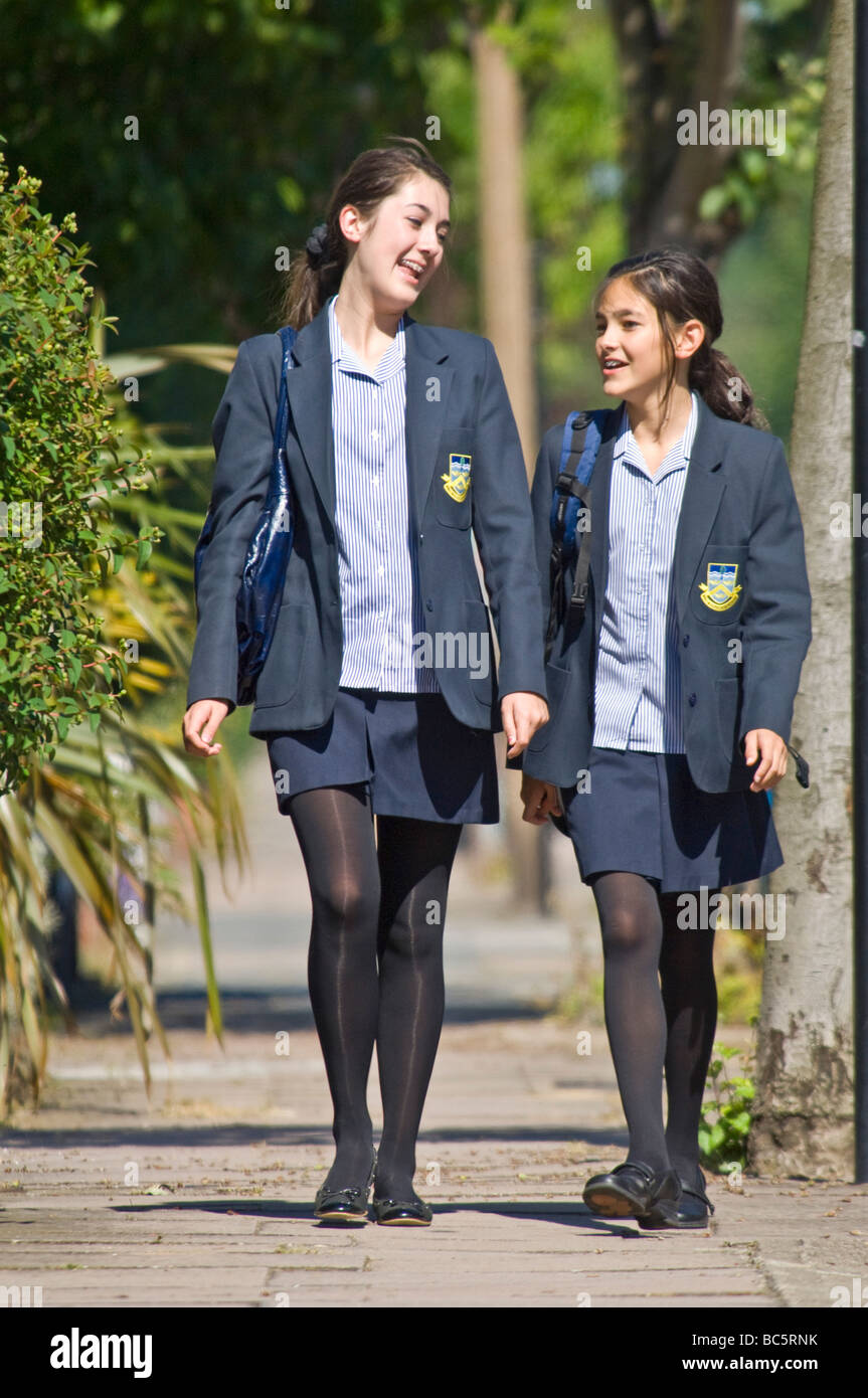 2 young caucasian girls (sisters 12 & 14) smiling and chatting while walking home/to school wearing their uniform. Stock Photo