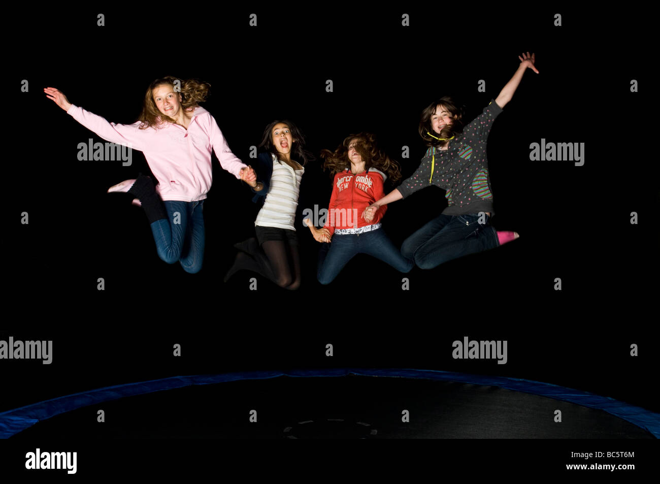 4 young early teens girl friends jumping on a trampoline at night on a birthday 'sleepover'. Stock Photo
