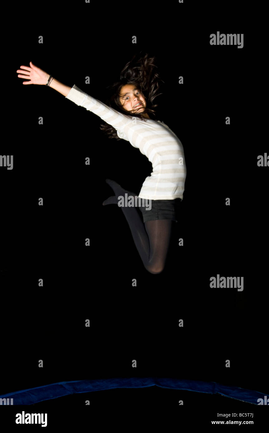 A young caucasian girl (12) in mid air jumping on a trampoline at night and laughing. Stock Photo