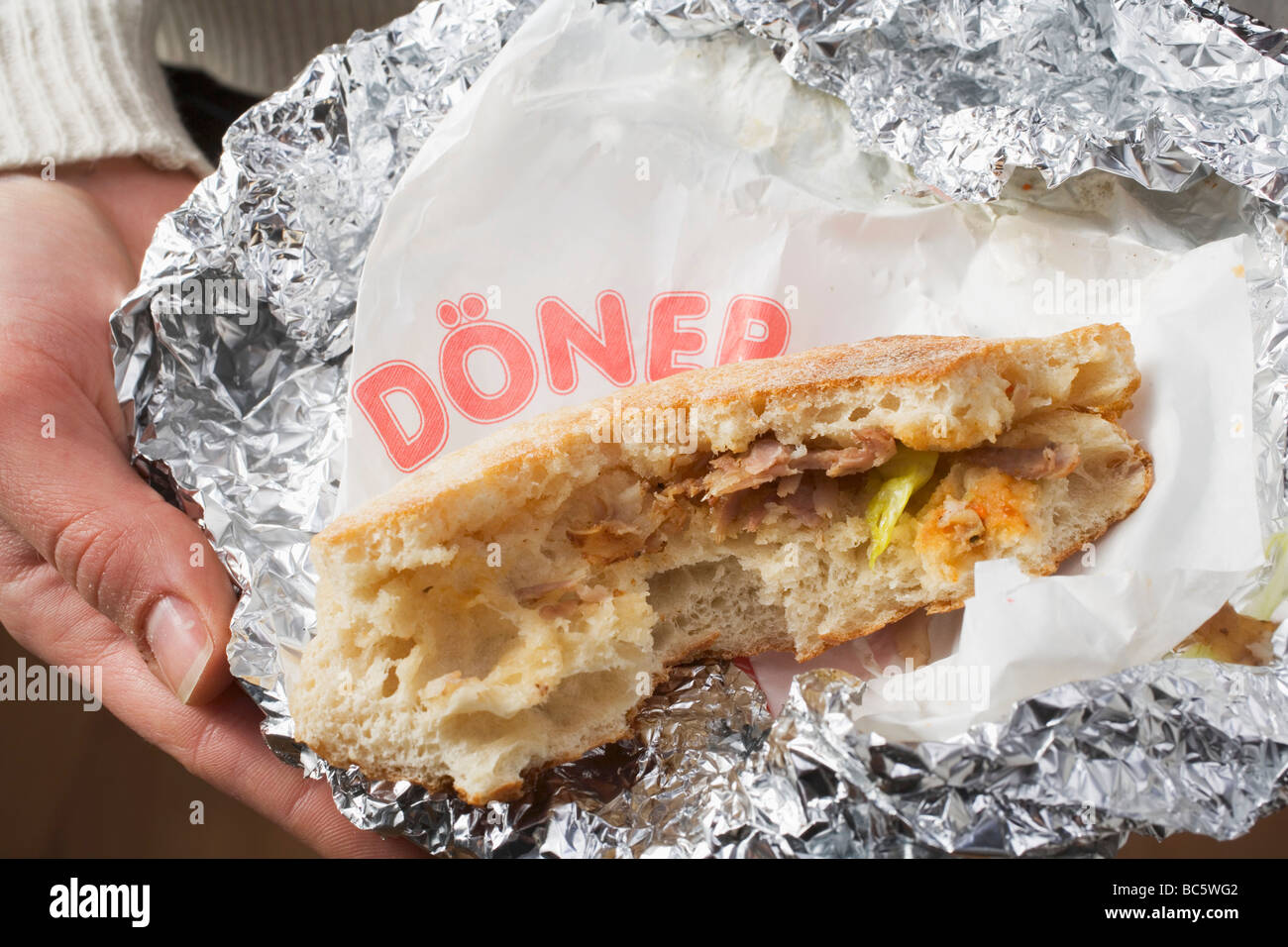 Person holding döner kebab, partly eaten, in aluminium foil Stock Photo