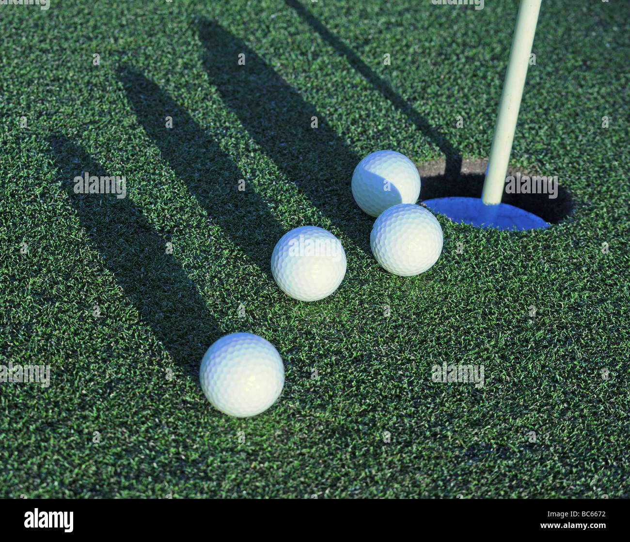 four golf balls rolling toward the cup with side shadows Stock Photo