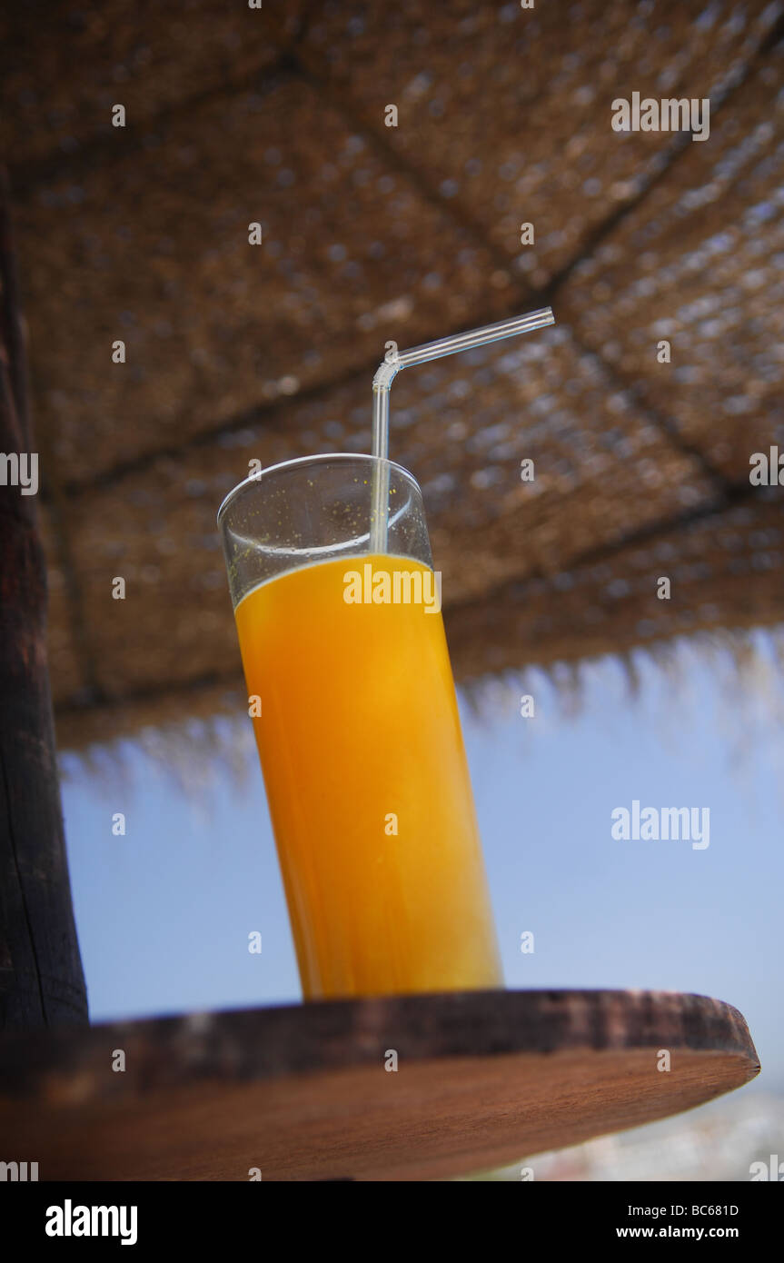 A cold glass of orange juice with straw rests on a table built on to a ...