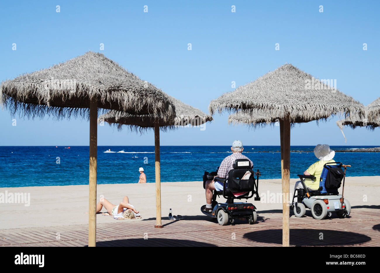 Couple on mobility scooters looking out to sea from Los Cristianos beach on Tenerife in The Canary Islands Stock Photo