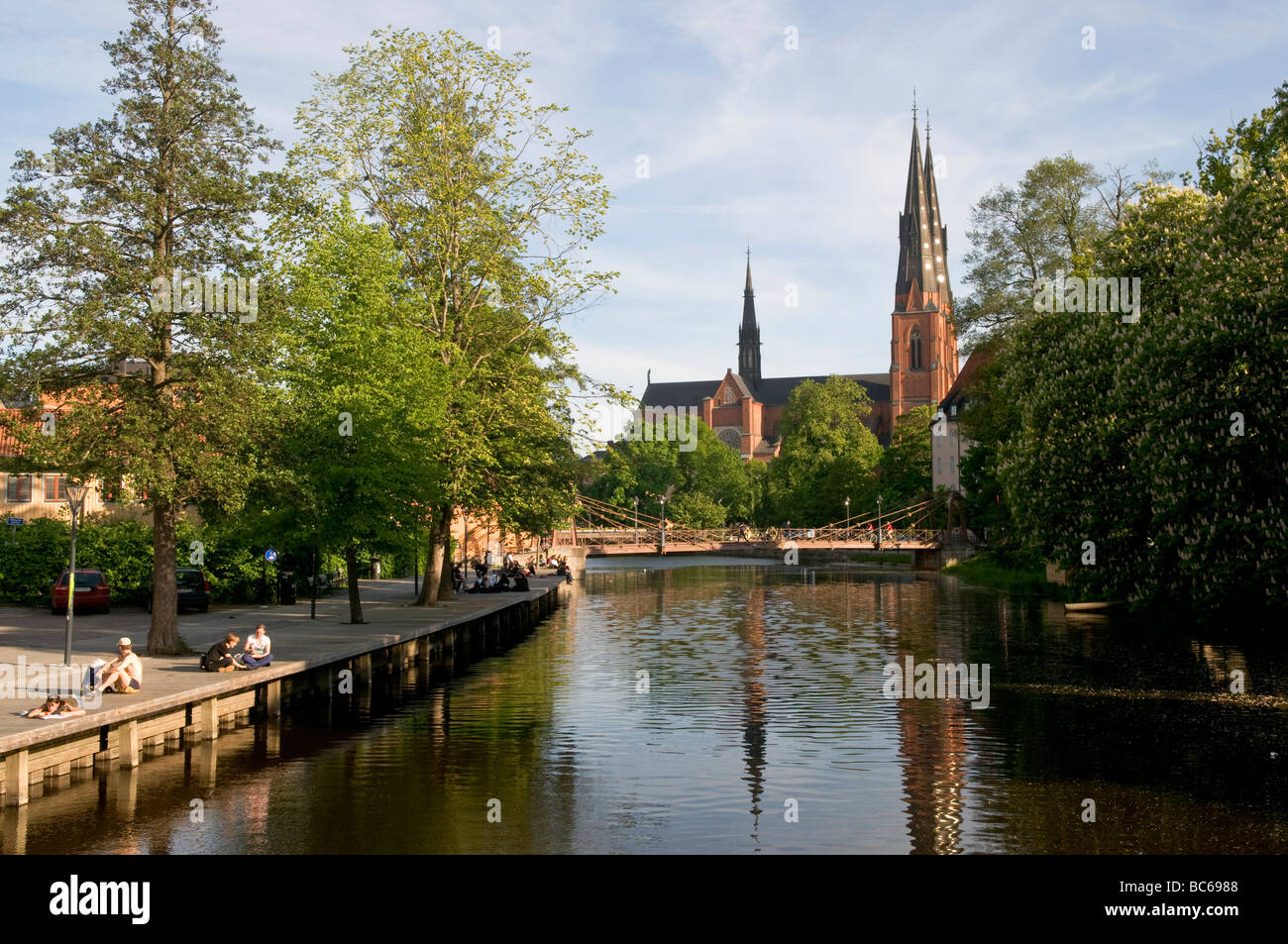People sitting on the banks of river Fyrisån, in Uppsala, Sweden, with Uppsala Cathedral in the background Stock Photo