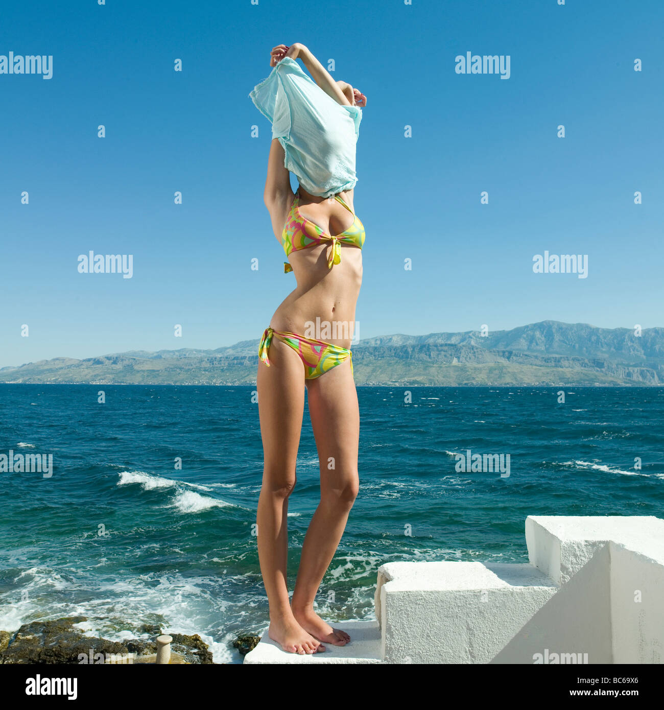 Young woman wearing bikini, taking off shirt by sea Stock Photo - Alamy.