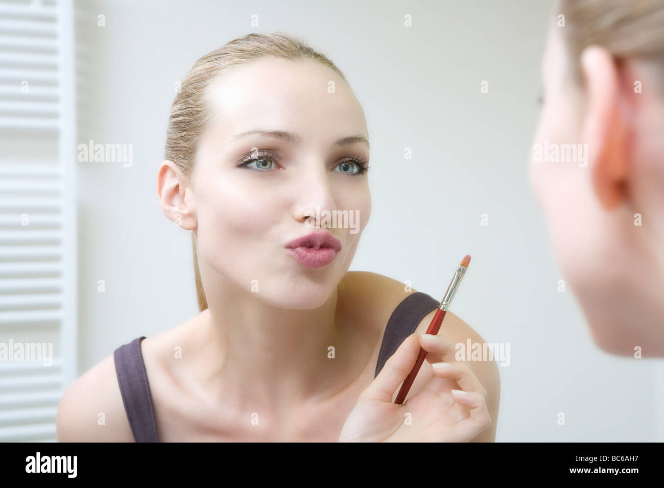 Young woman holding lip brush, puckering lips Stock Photo Alamy