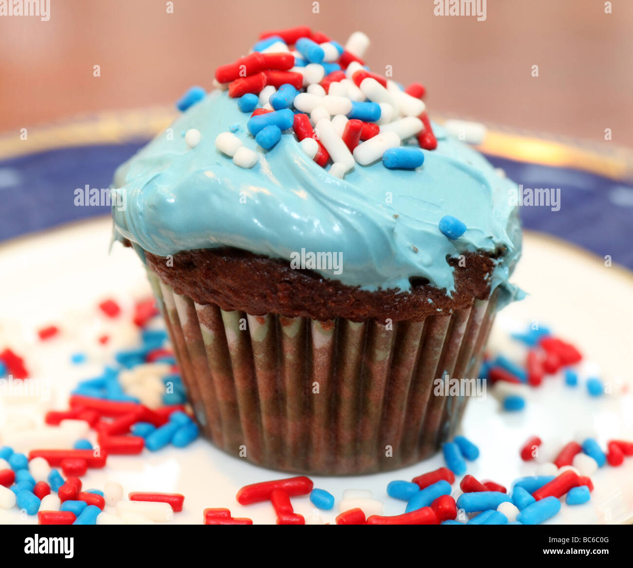 Blue frosted chocolate cupcake, decorated with red, white, and blue sprinkles, placed on royal blue Wedgewood china plate Stock Photo