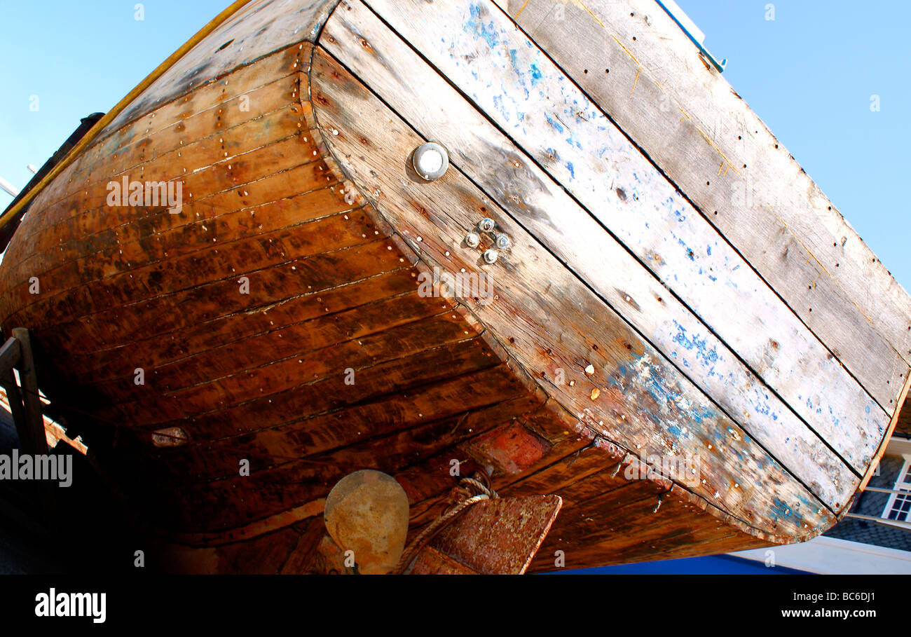 Hull view of a wooden boat in dry dock for repair, with blue sky background. Stock Photo