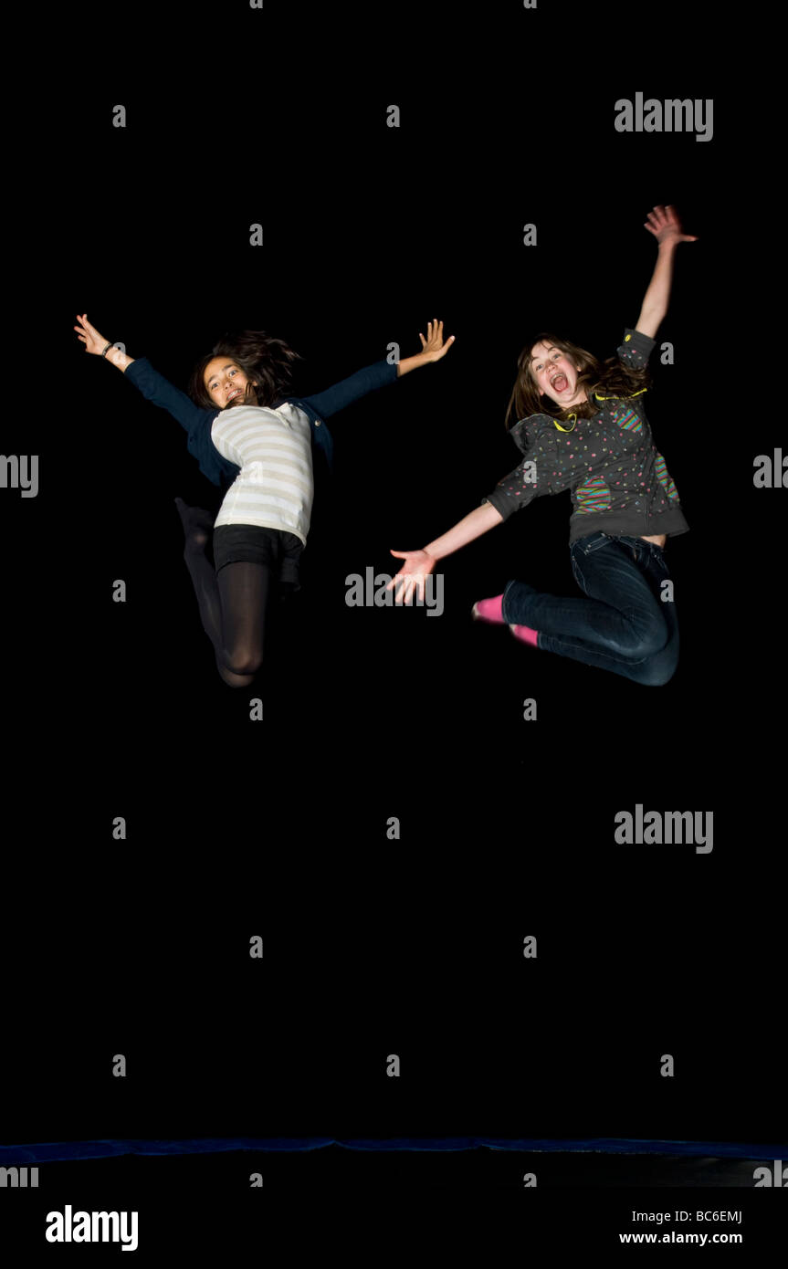 2 young early teens girl friends jumping on a trampoline while laughing at night on a birthday 'sleepover'. Stock Photo