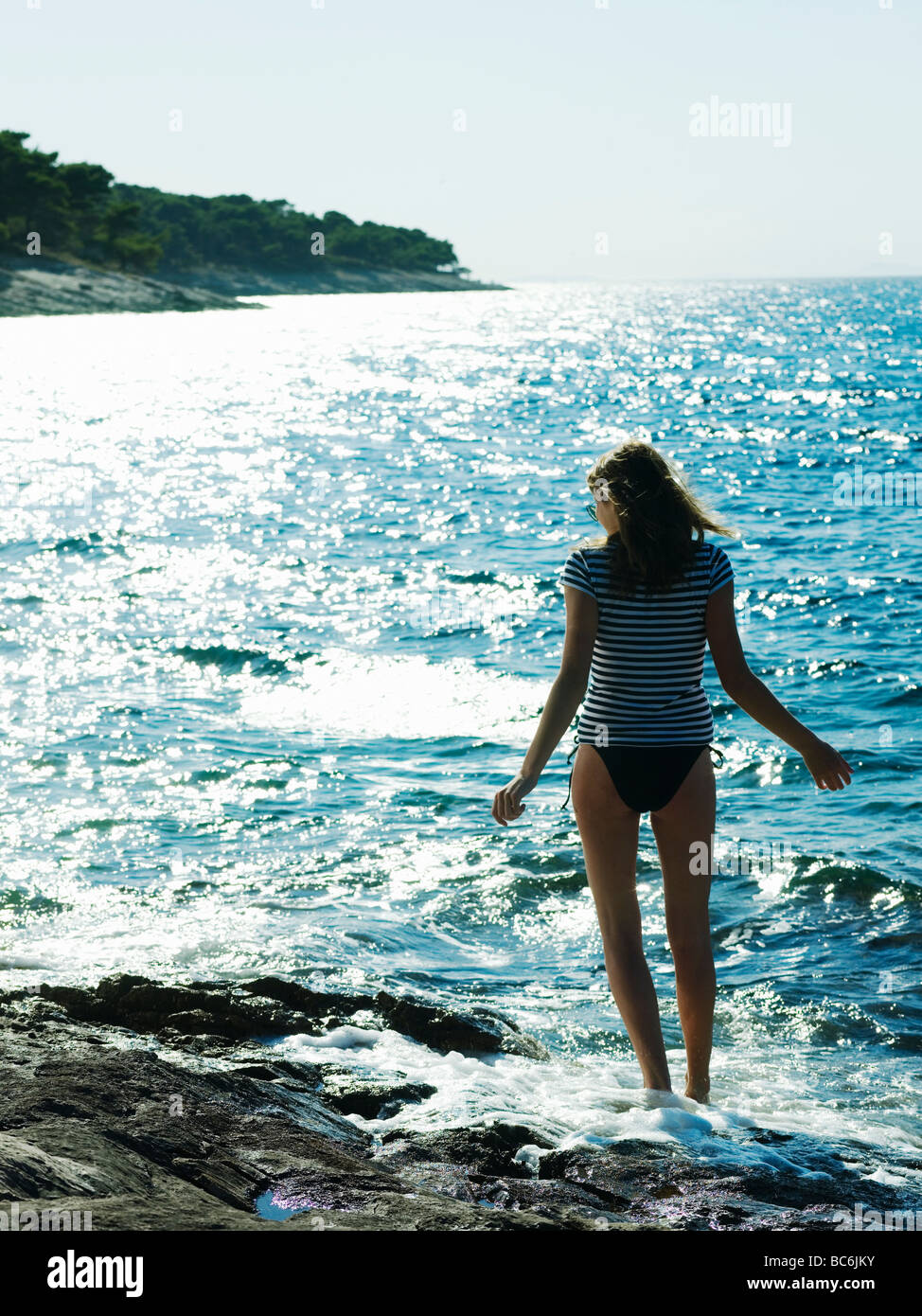 Young woman wearing bikini, taking off shirt by sea Stock Photo