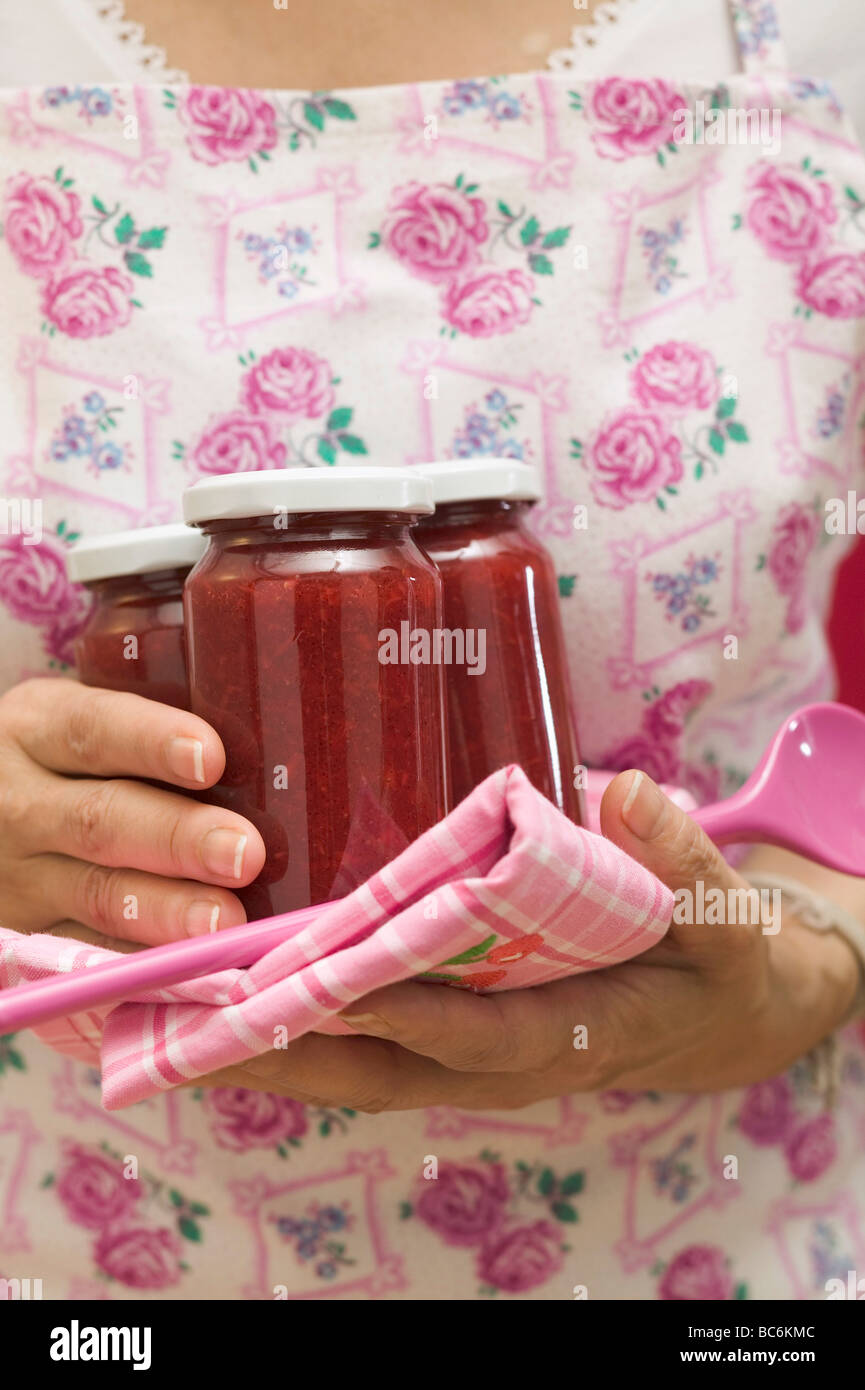 Woman holding jars of jam, tea towel and kitchen spoon - Stock Photo