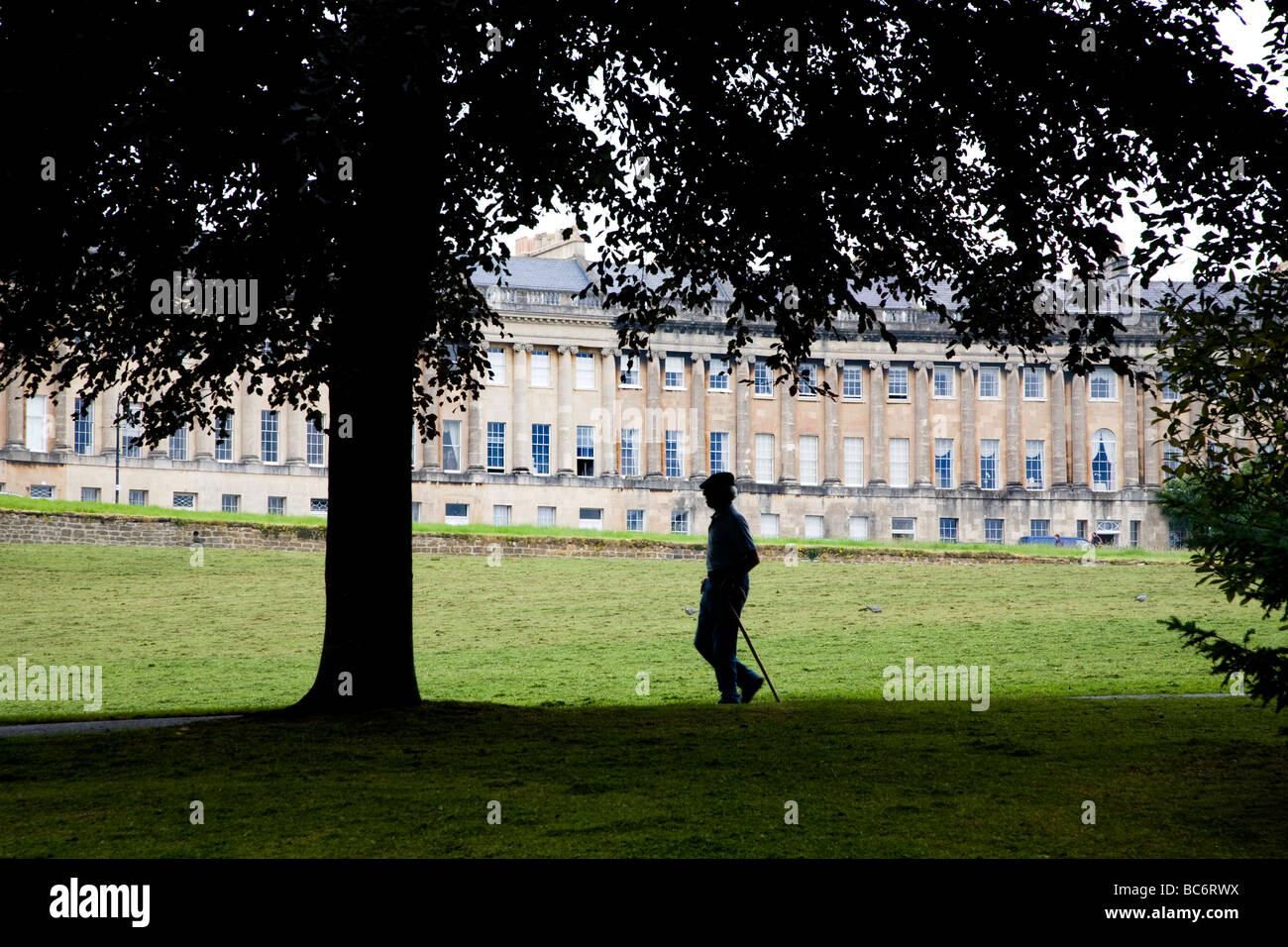 silhouette of a man walking in front of The Royal Crescent in Bath, england, WITH OPEN AREAS OF LAWN AND TREES Stock Photo