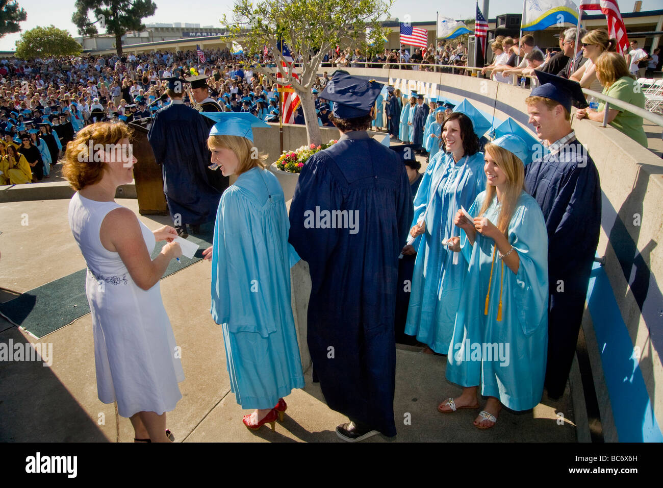 Wearing cap and gown graduating high school seniors give their names