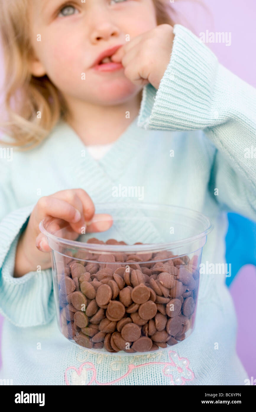 Small girl eating chocolate buttons out of plastic tub Stock Photo - Alamy
