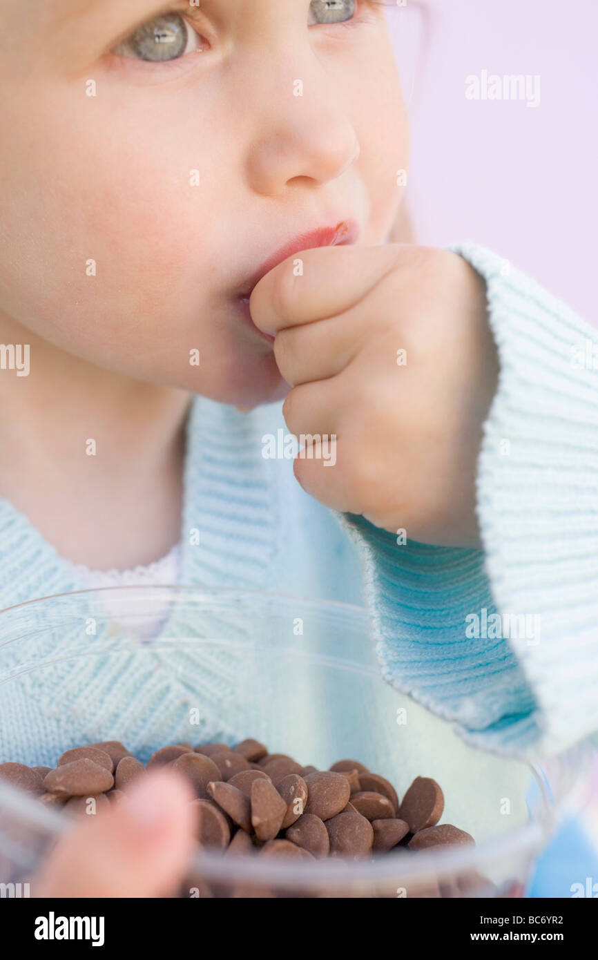 Small girl eating chocolate buttons out of plastic tub Stock Photo - Alamy