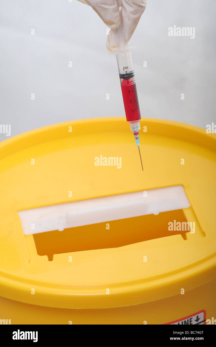 Nurse disposing of bloodfilled syringe in hospital "sharps" disposal