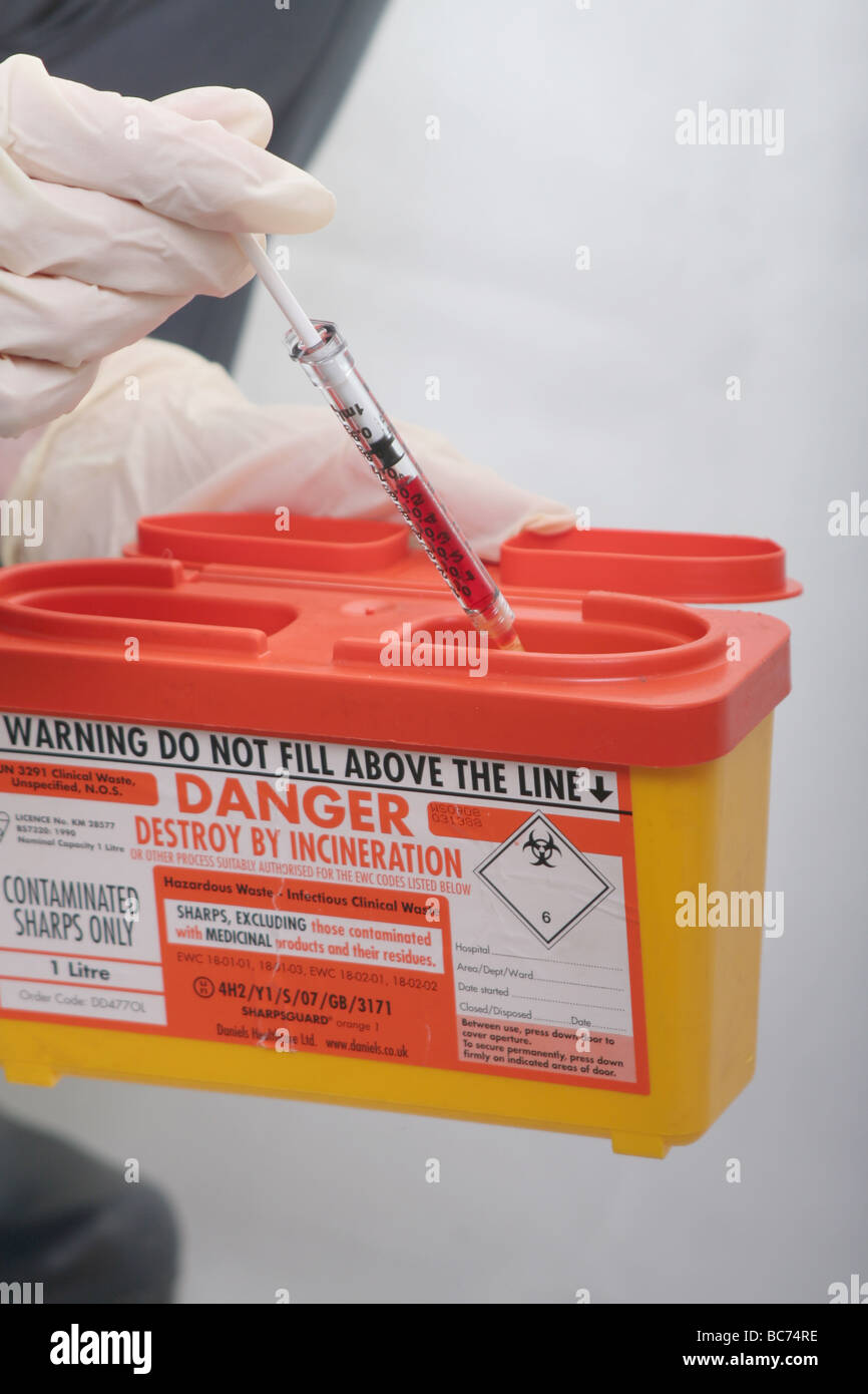 Nurse disposing of bloodfilled syringe in hospital "sharps" disposal