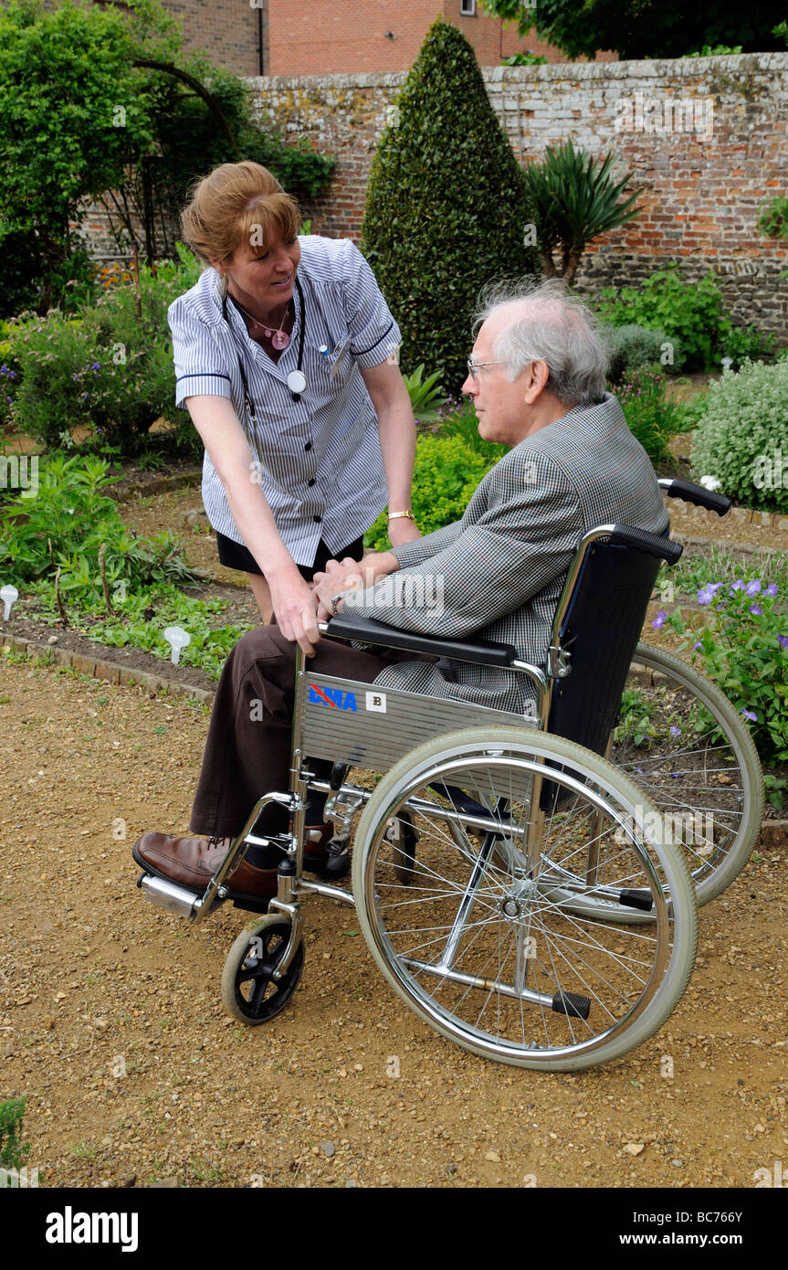 Nurse carer attending to elderly male patient in a wheelchair Stock