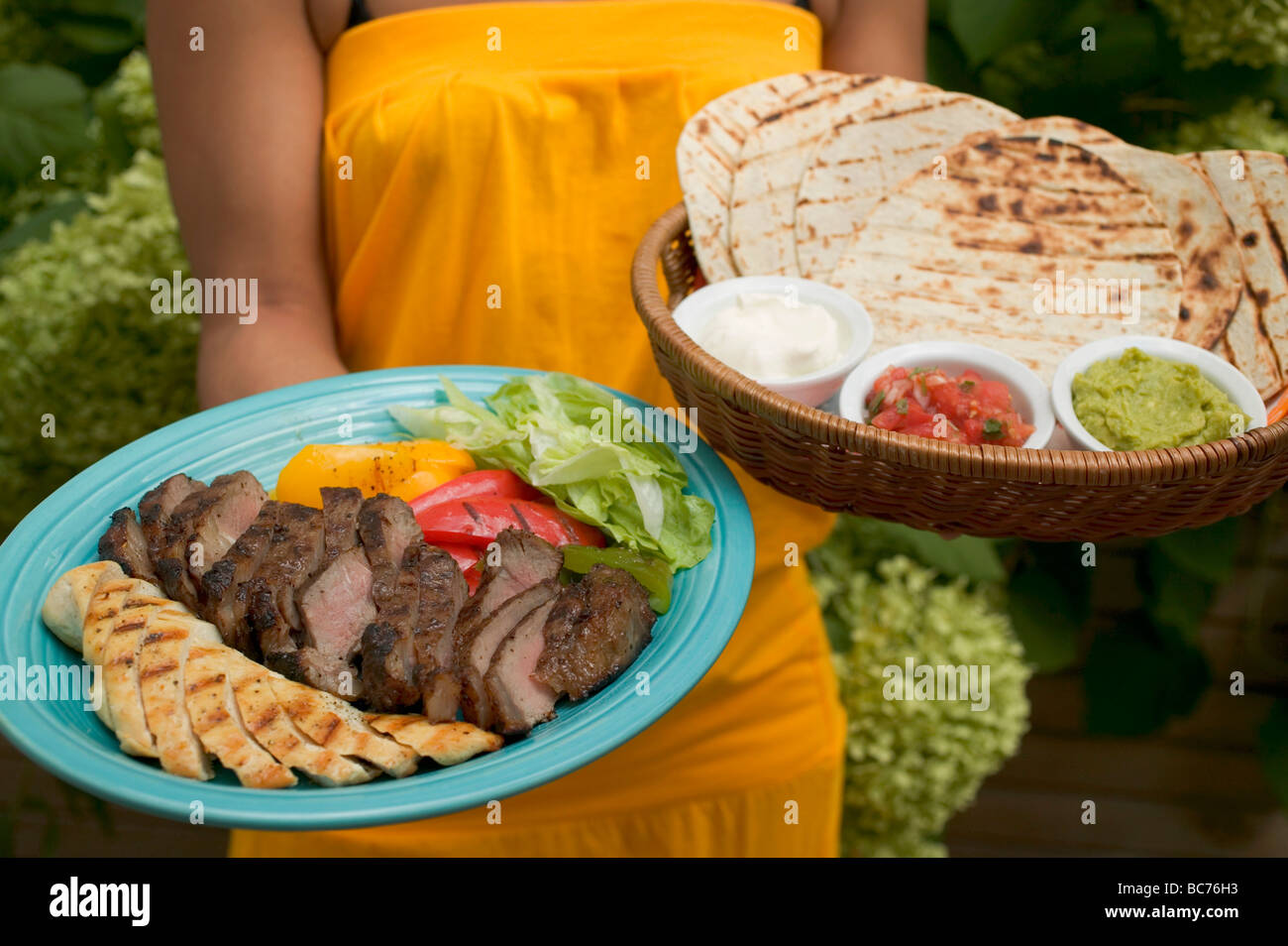 Woman serving Asian platter and basket of accompaniments - Stock Photo