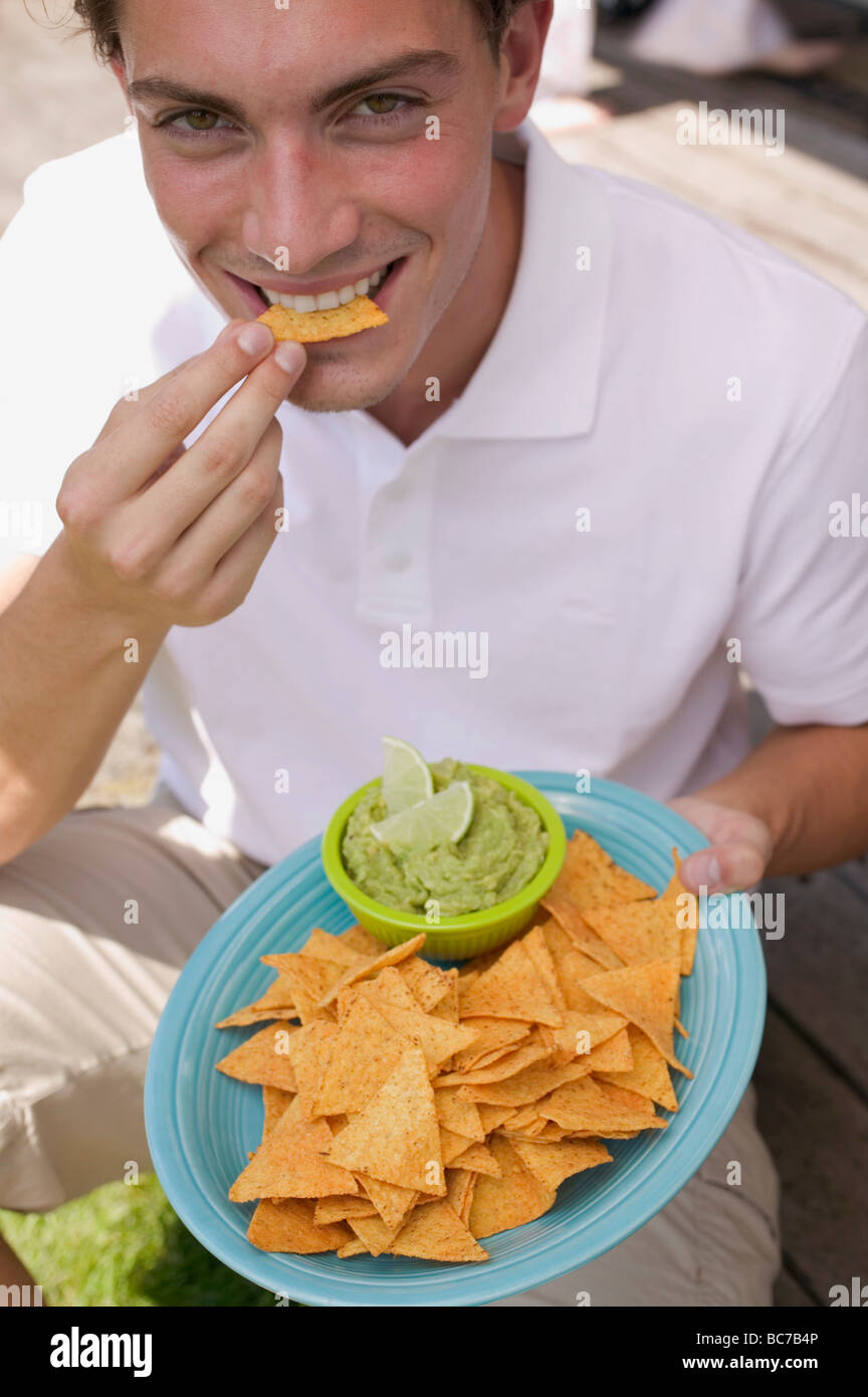 Young man eating tortilla chips with guacamole Stock Photo Alamy